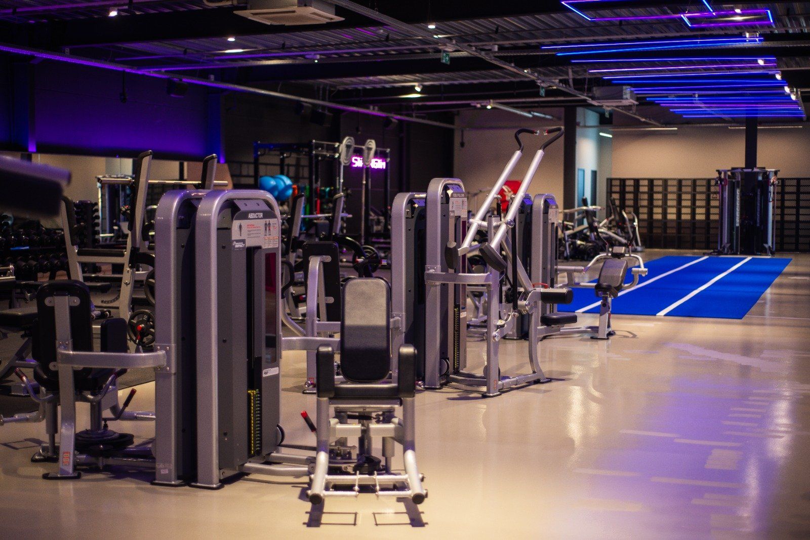 Een gymzaal vol met fitnessapparatuur en een blauwe baan.