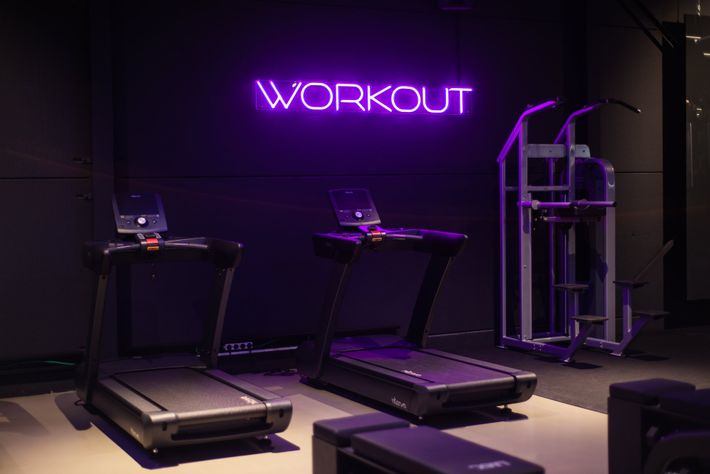 een sportschool met loopbanden en een neonbord met de tekst 'workout