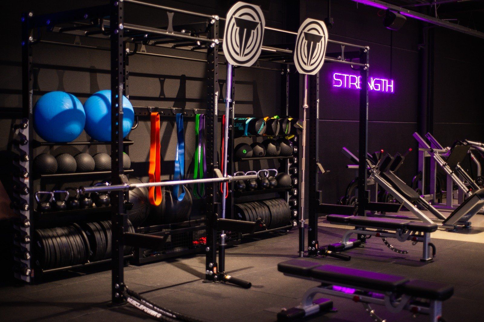 Een sportschool met veel apparatuur en een neonbord met de tekst 'kracht'.