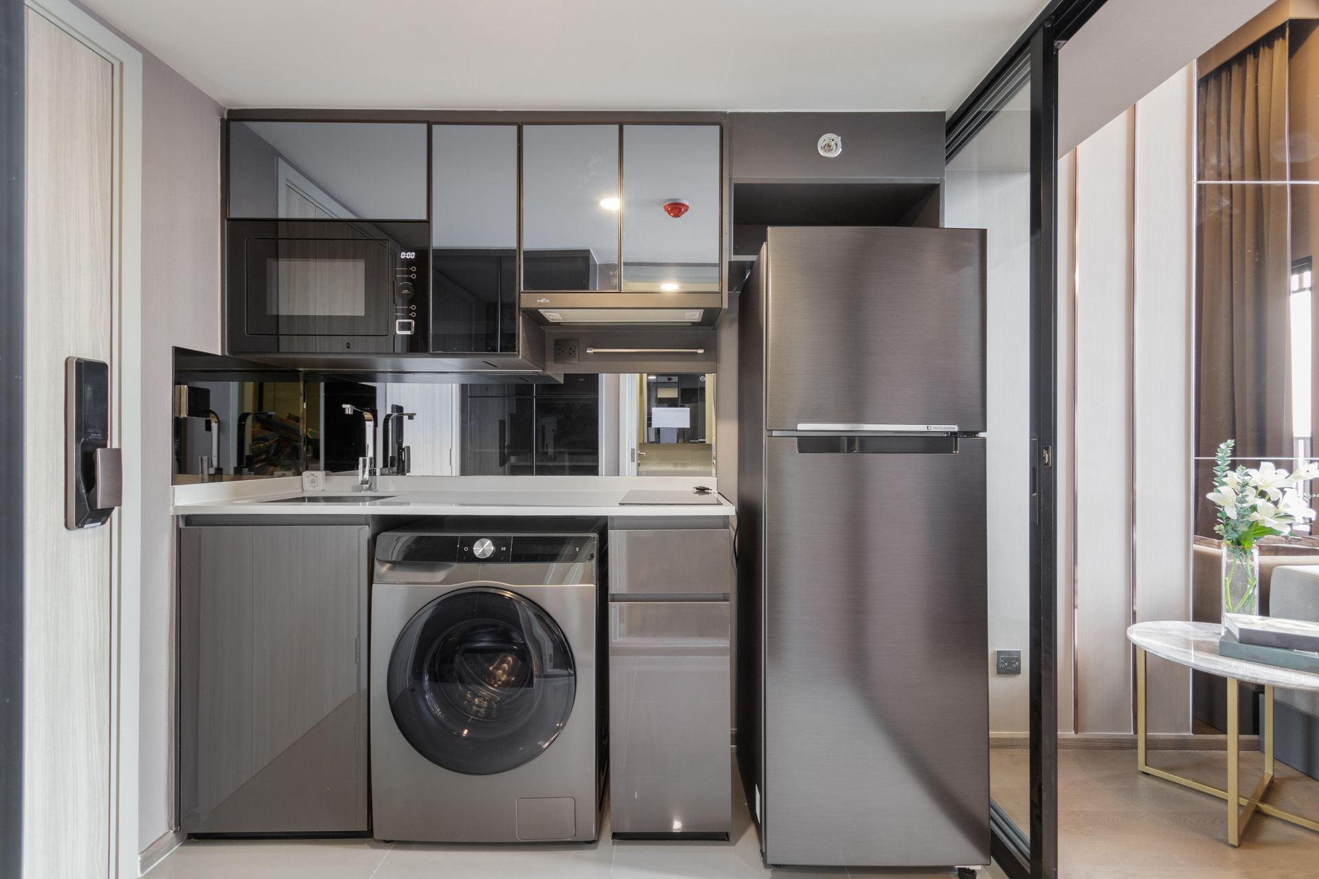 Modern, small kitchen with a washing machine, refrigerator, and mirrored cabinets.