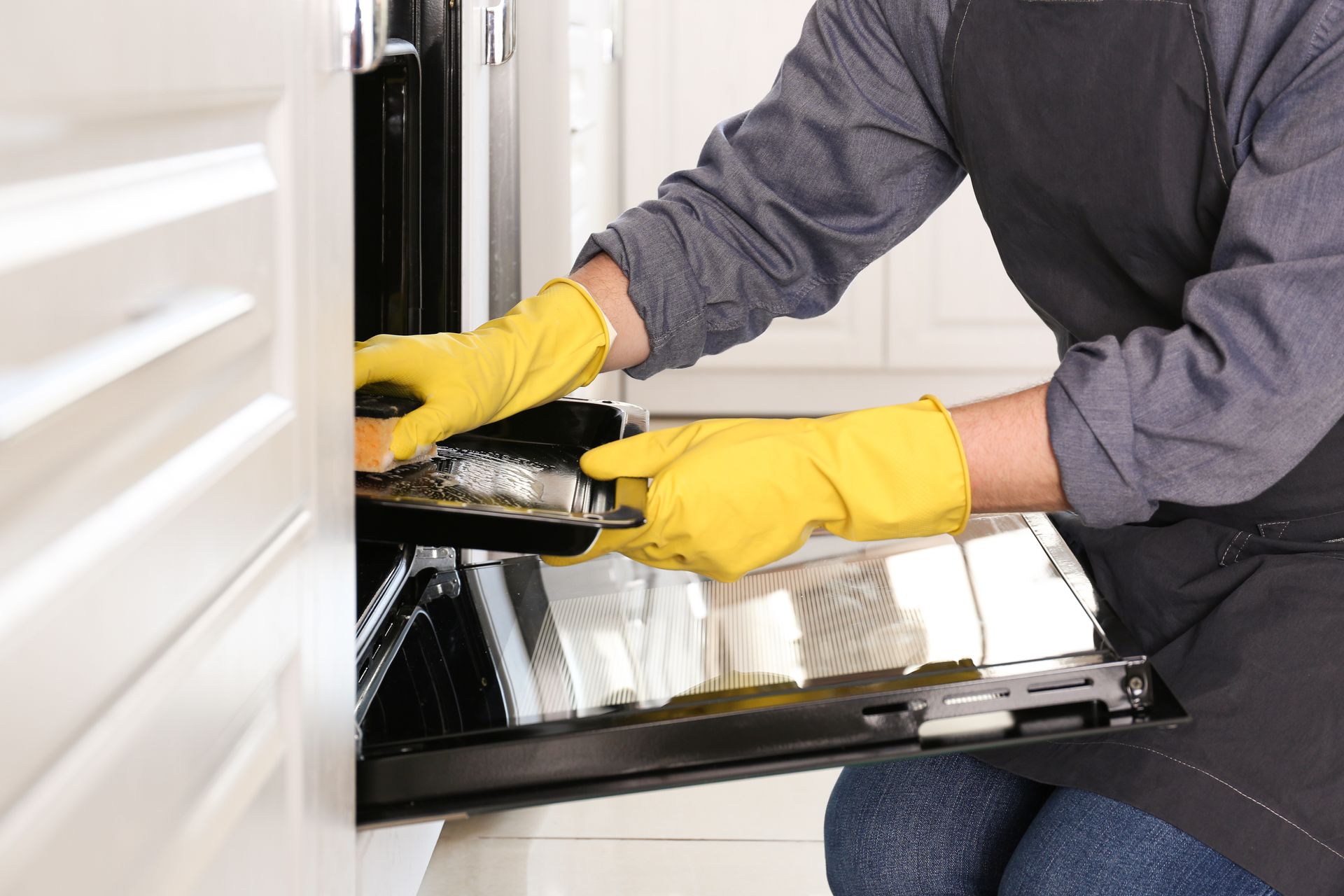 Person wearing yellow gloves and apron cleaning an oven.