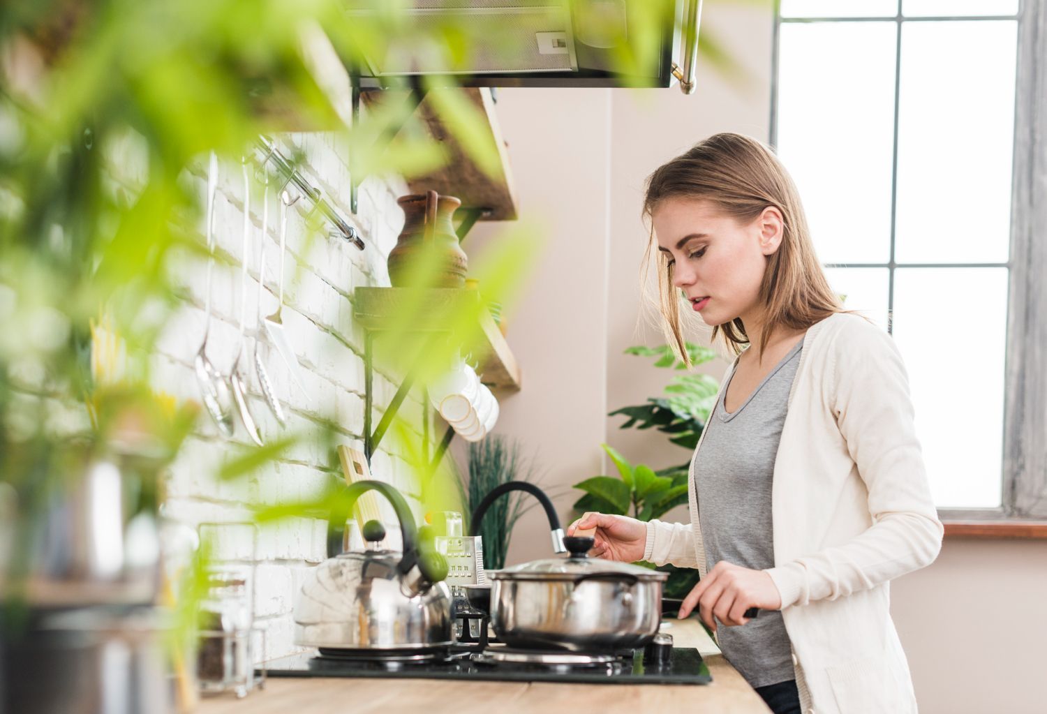 A woman is standing in a kitchen cooking food in a pot.