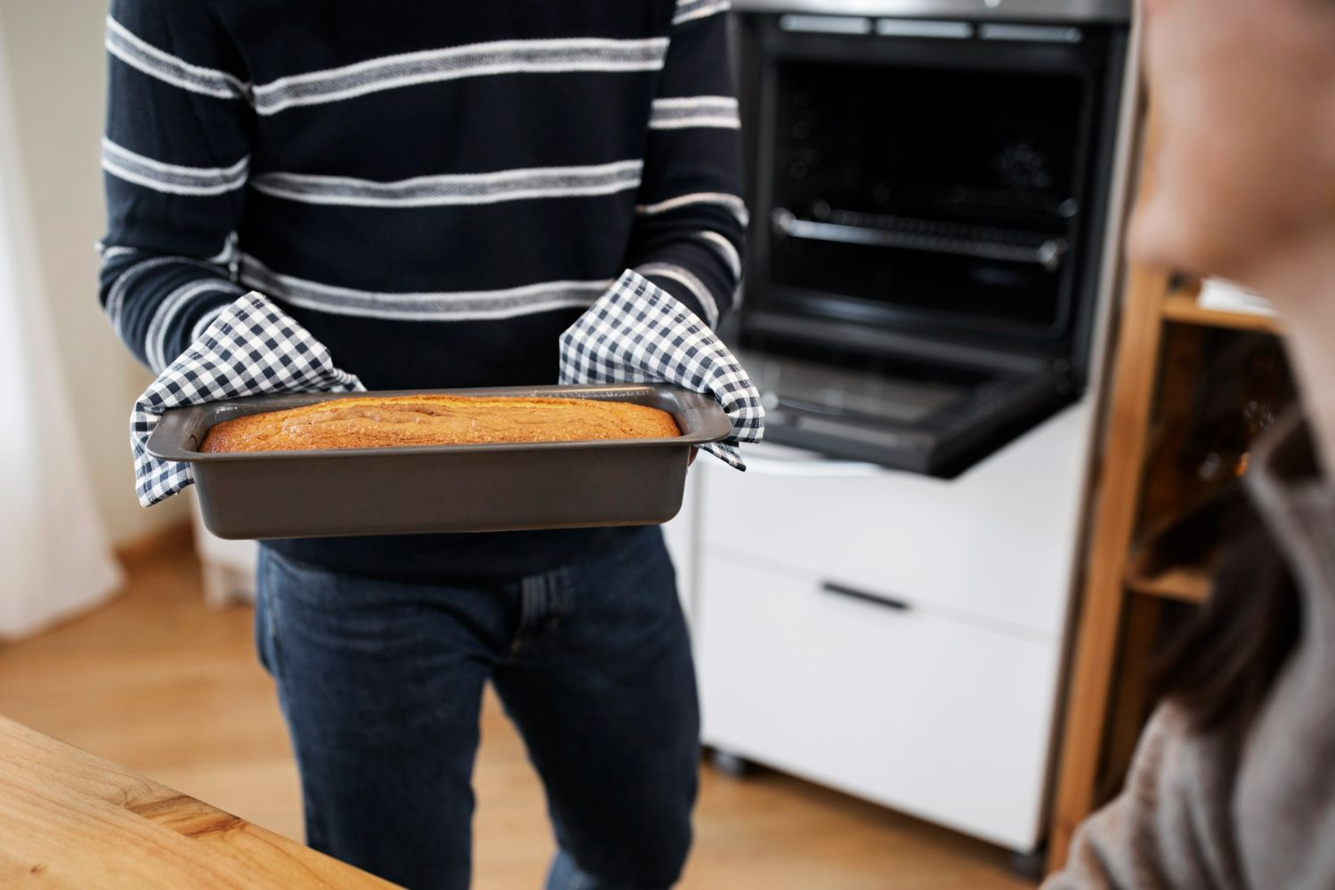 A man is holding a loaf of bread in front of an oven.