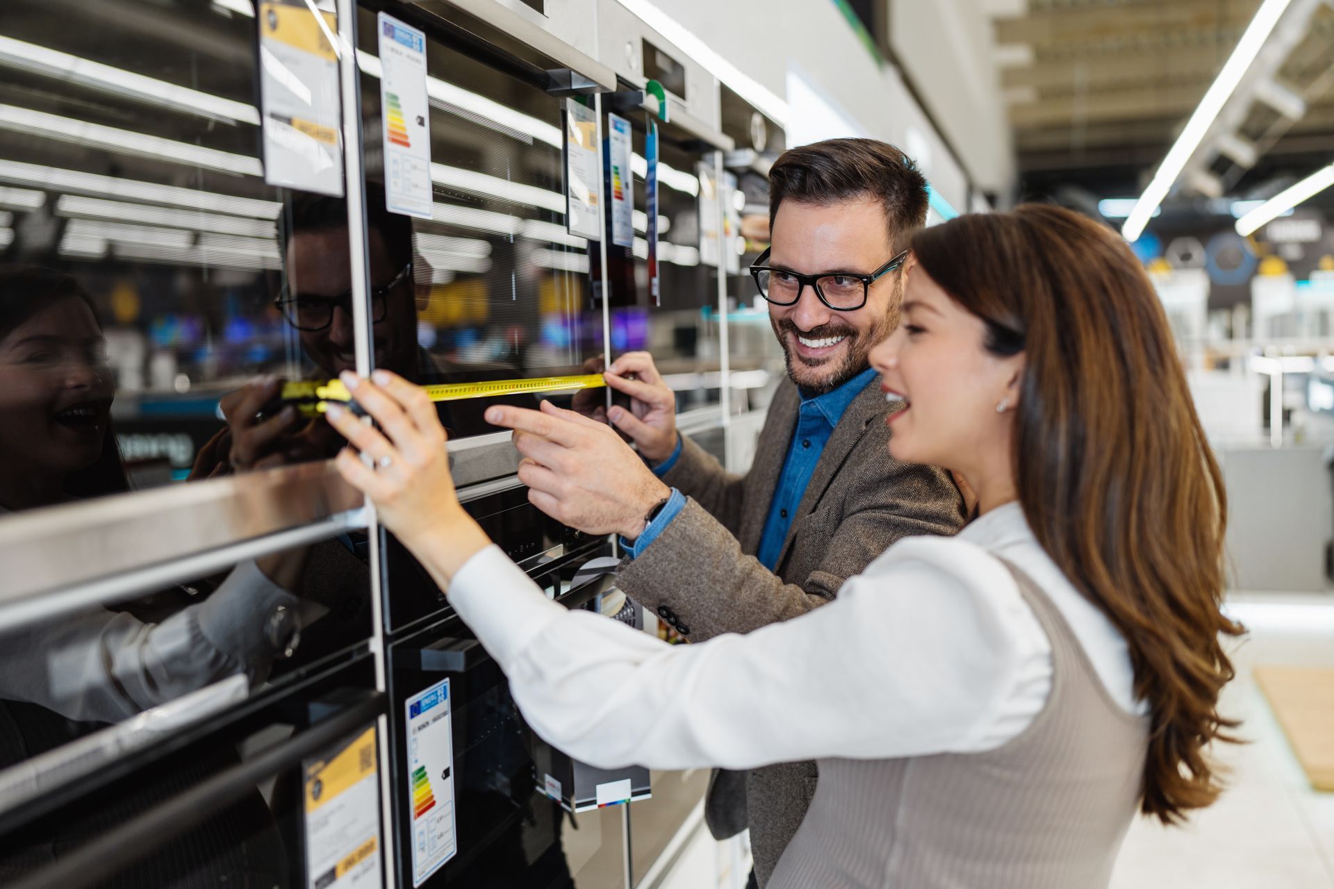 Couple shopping for appliances in a store, pointing and smiling at an oven.