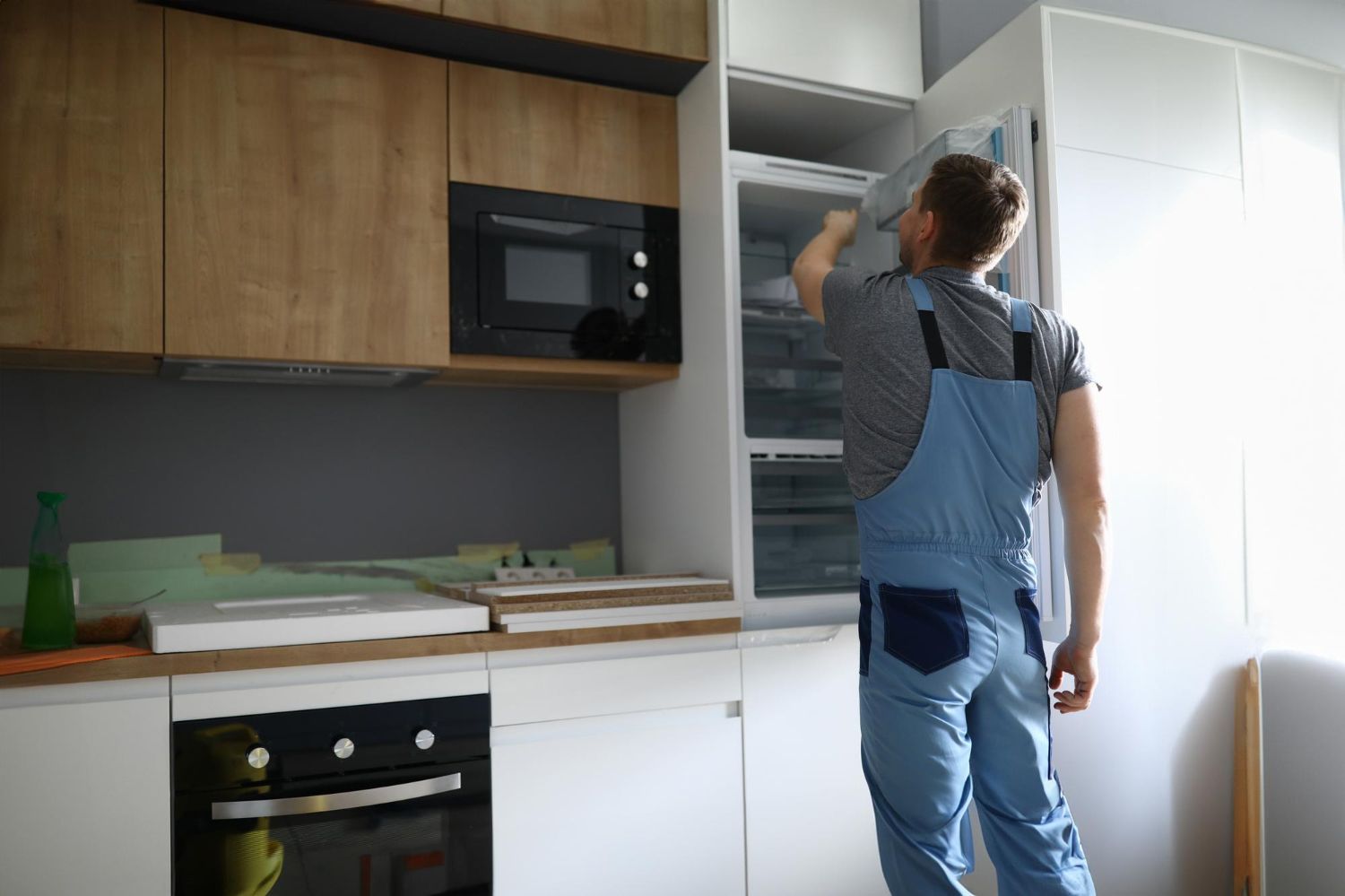 A man in overalls is opening a refrigerator in a kitchen.
