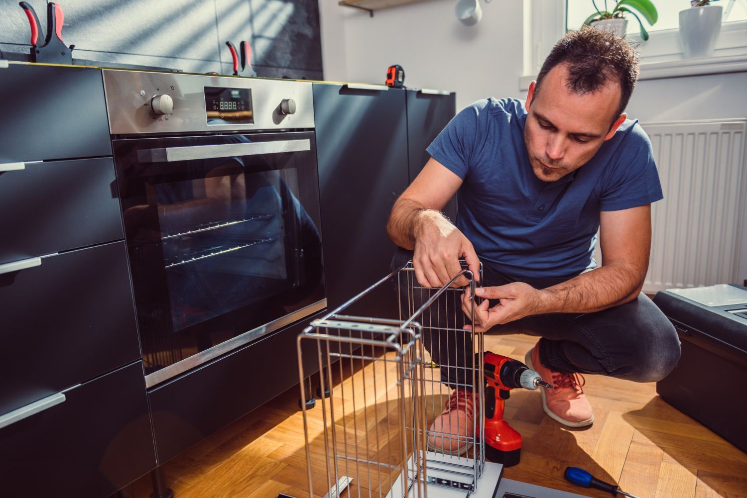 A man is kneeling on the floor in a kitchen fixing a basket.