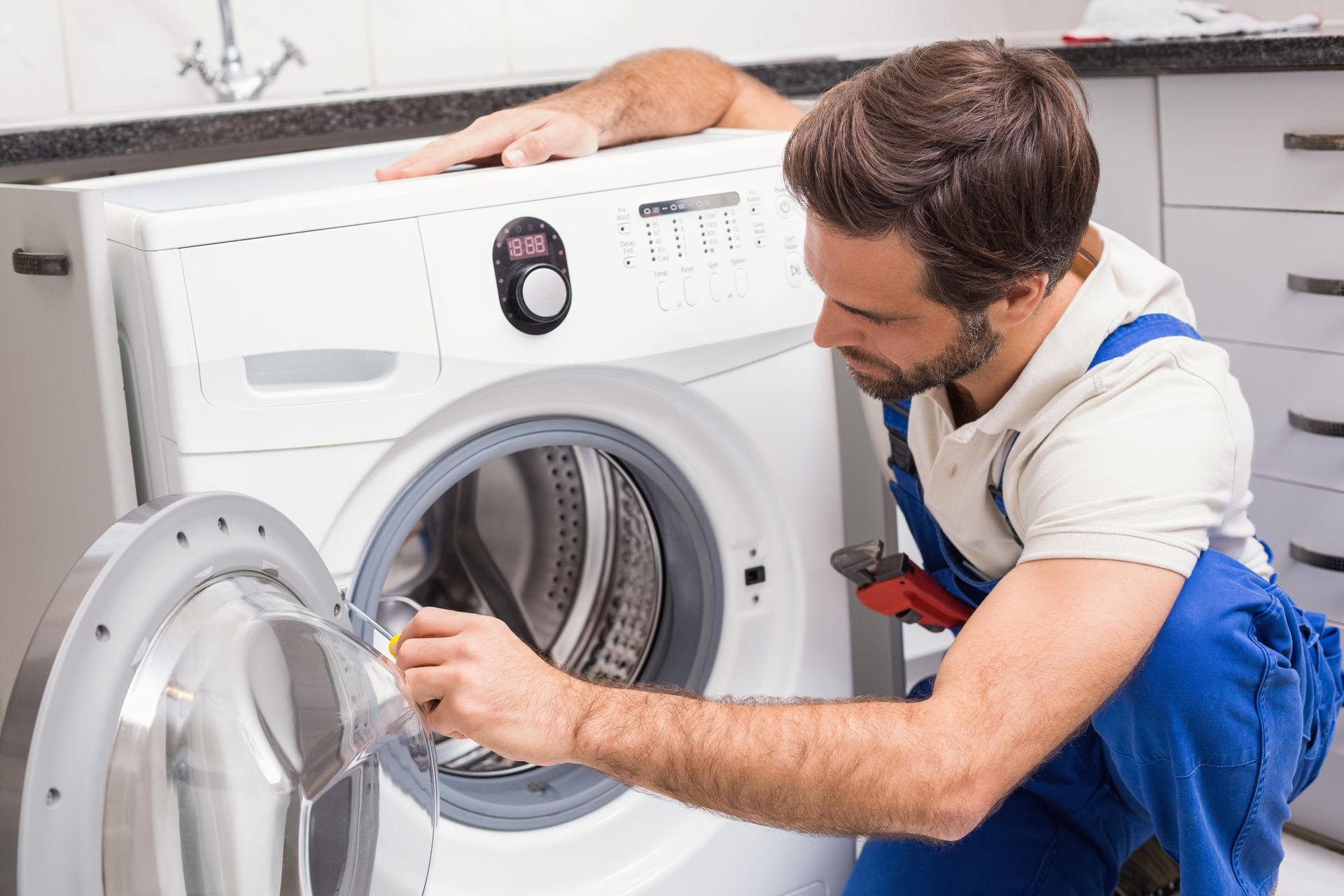 A man is fixing a washing machine in a kitchen.
