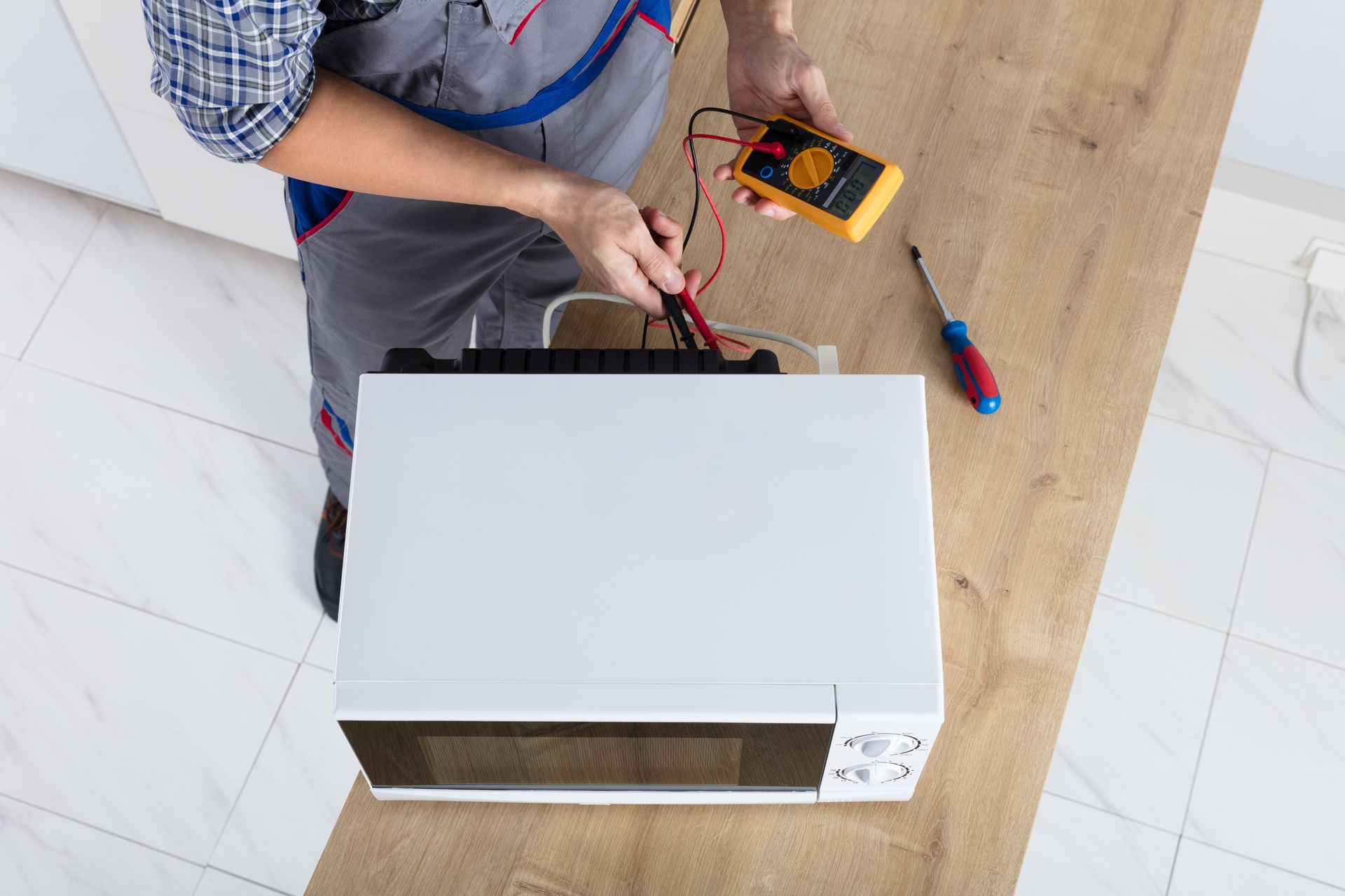 A man is fixing a microwave with a multimeter.