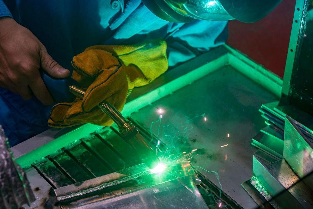 A Man Is Welding A Piece Of Metal With A Green Light Behind Him — Kaplan Engineering Pty Ltd In Bowen, QLD