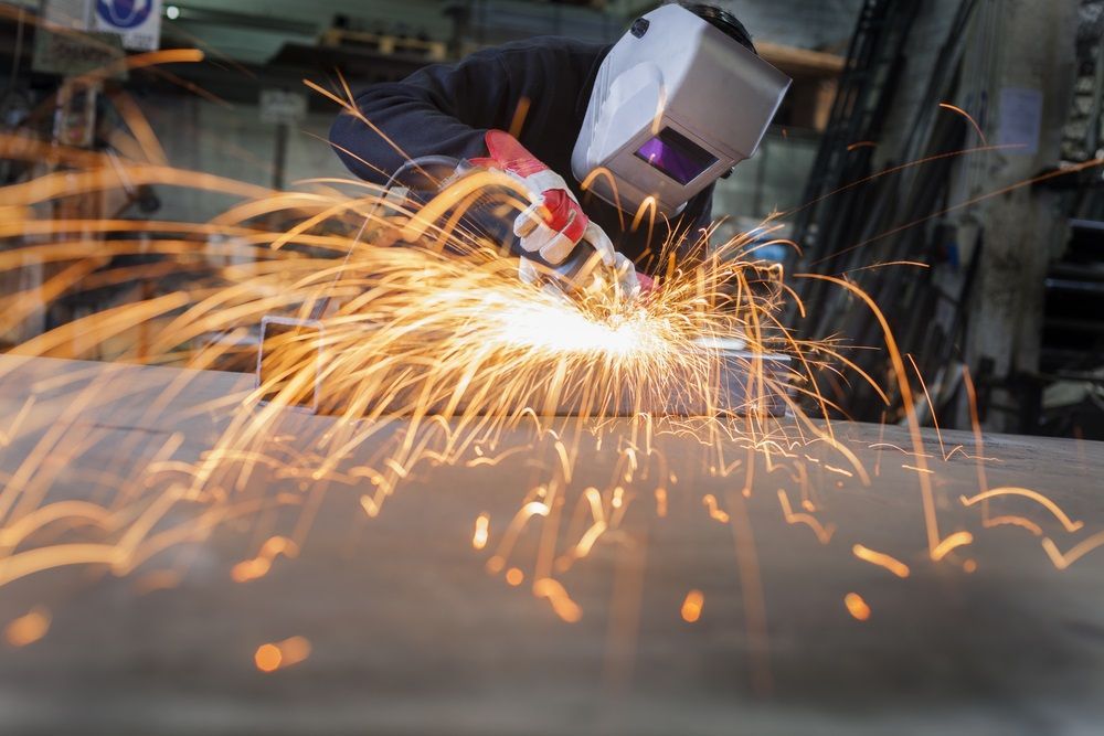 A Man Wearing A Welding Helmet Is Grinding A Piece Of Metal In A Factory — Kaplan Engineering Pty Ltd In Airlie Beach, QLD