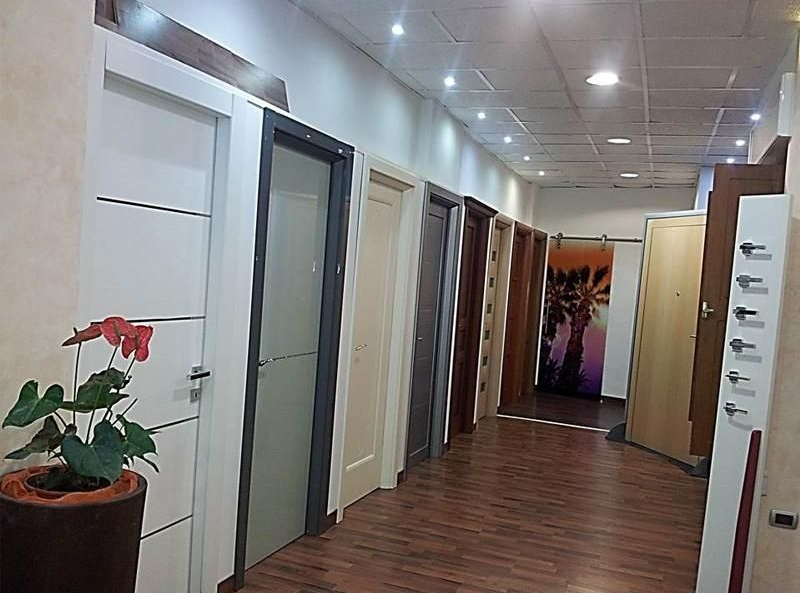 Corridoio con campioni di porte in vari colori e stili; una pianta si trova sulla sinistra.