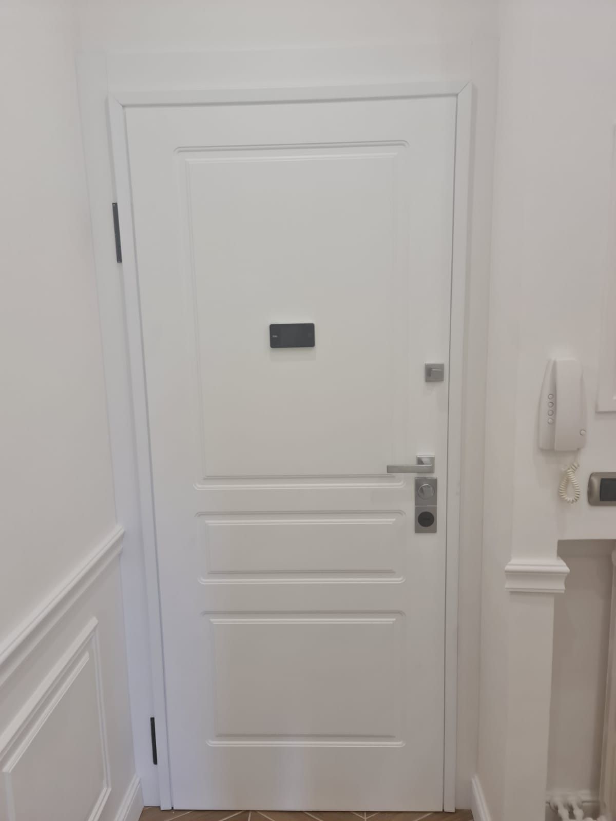 Porta interna bianca con un piccolo oggetto rettangolare scuro al centro della porta.