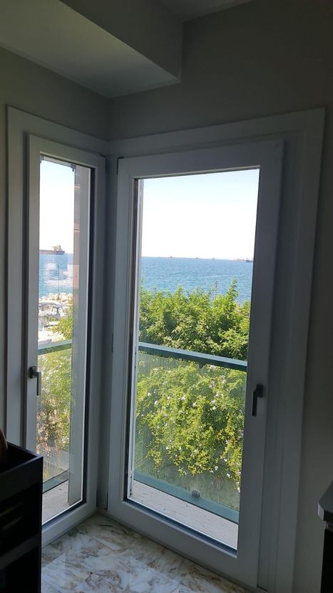Finestra angolare con vista mare; sono visibili alberi e balcone.