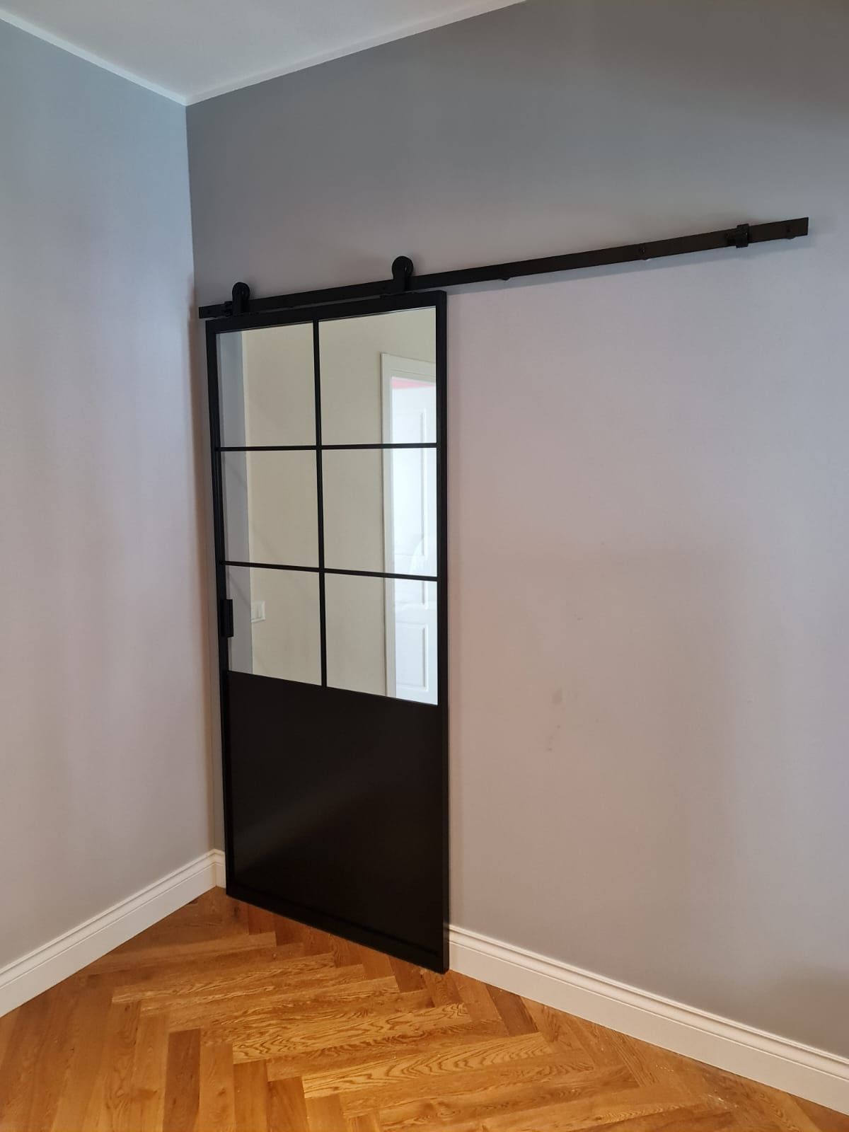 Porta scorrevole in vetro nero con telaio in metallo su pareti grigie e pavimento in legno.