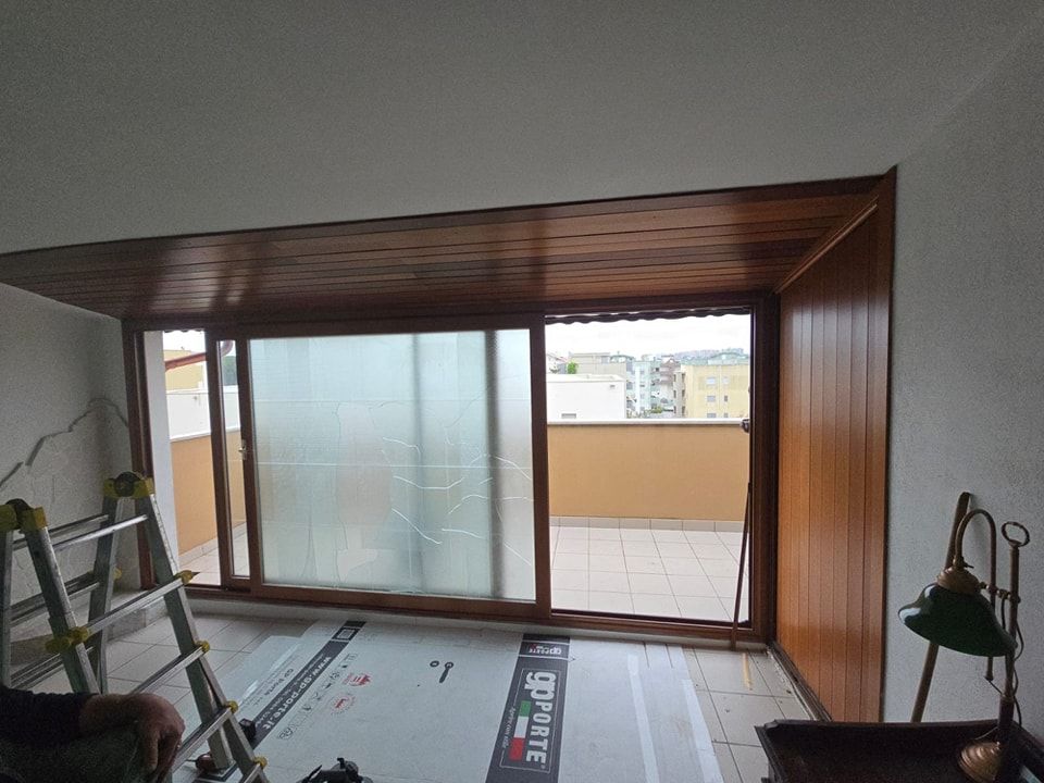 Ristrutturazione degli interni con porta scorrevole in vetro che si apre su un balcone. Rifiniture e pannelli in legno marrone.