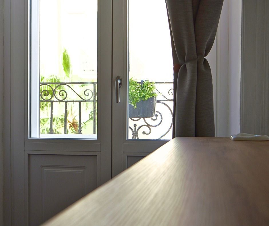Ingresso con vista sul balcone: verde, ringhiera nera decorata, pianta in vaso e una tenda scostata.