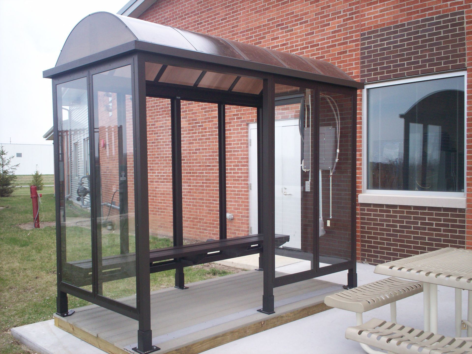 A bus stop with a picnic table in front of a brick building