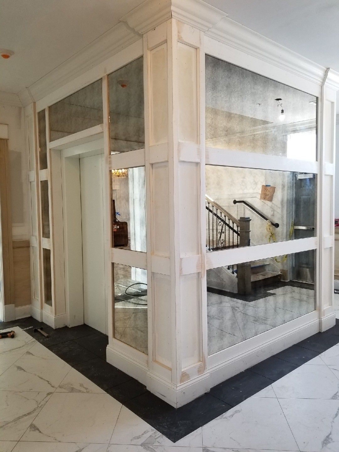 A hallway with a mirrored wall and a staircase in the background.