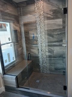 A bathroom with a walk in shower with a glass door and a window.