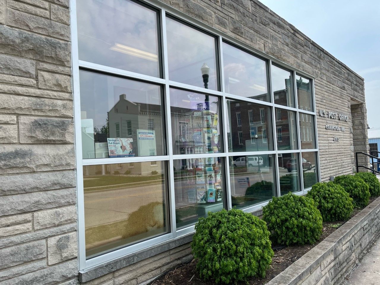 A brick building with a lot of windows and bushes in front of it.