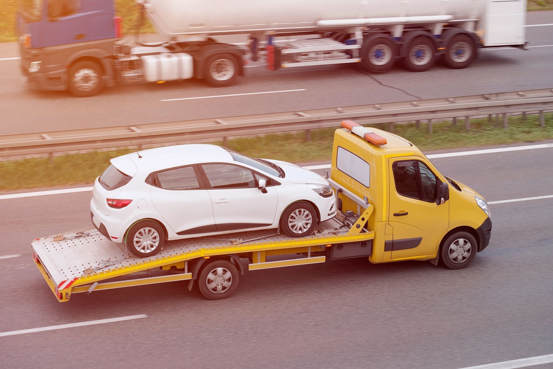 Una grúa está remolcando un coche blanco por una autopista.