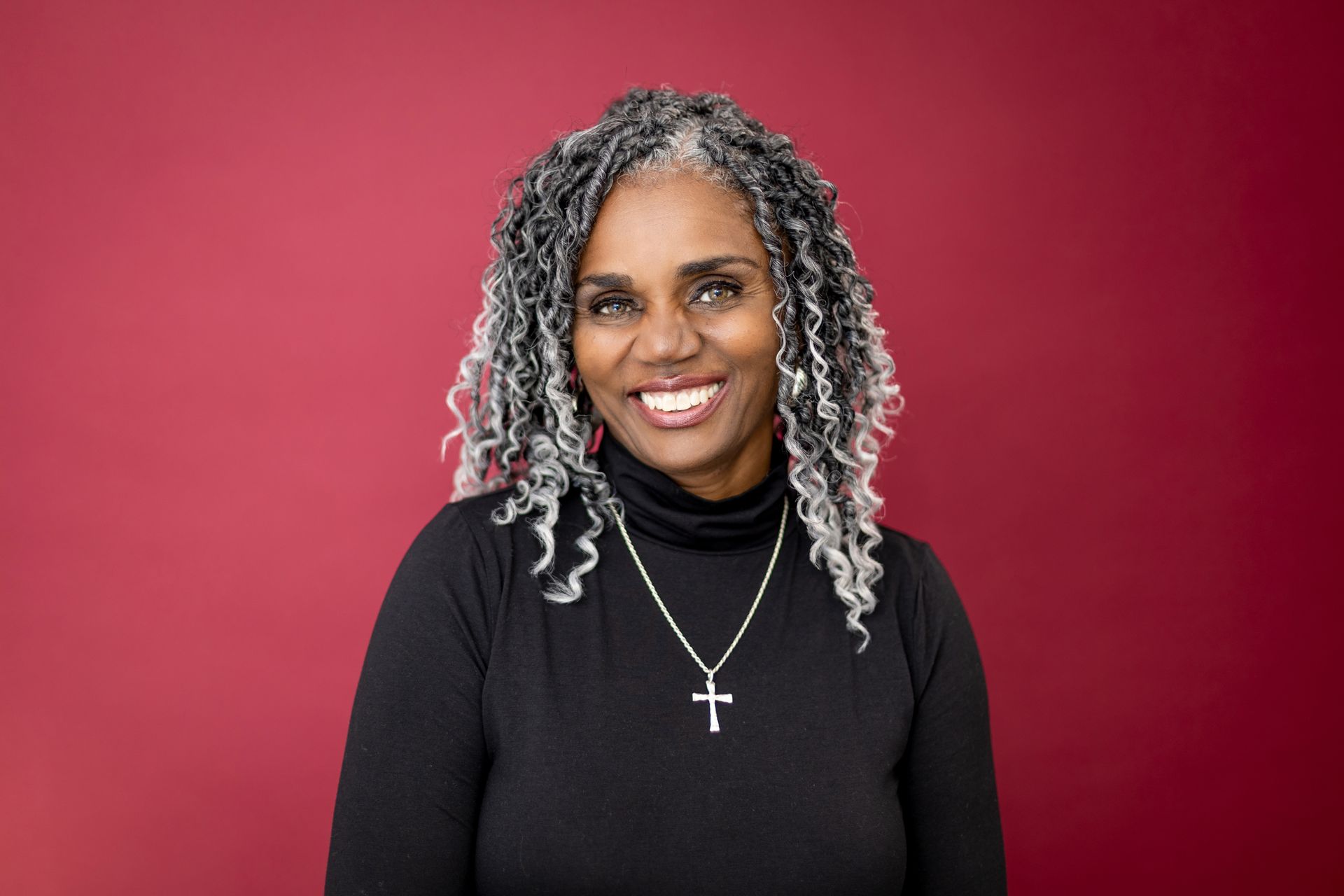 A woman with gray hair is wearing a black turtleneck and a cross necklace.