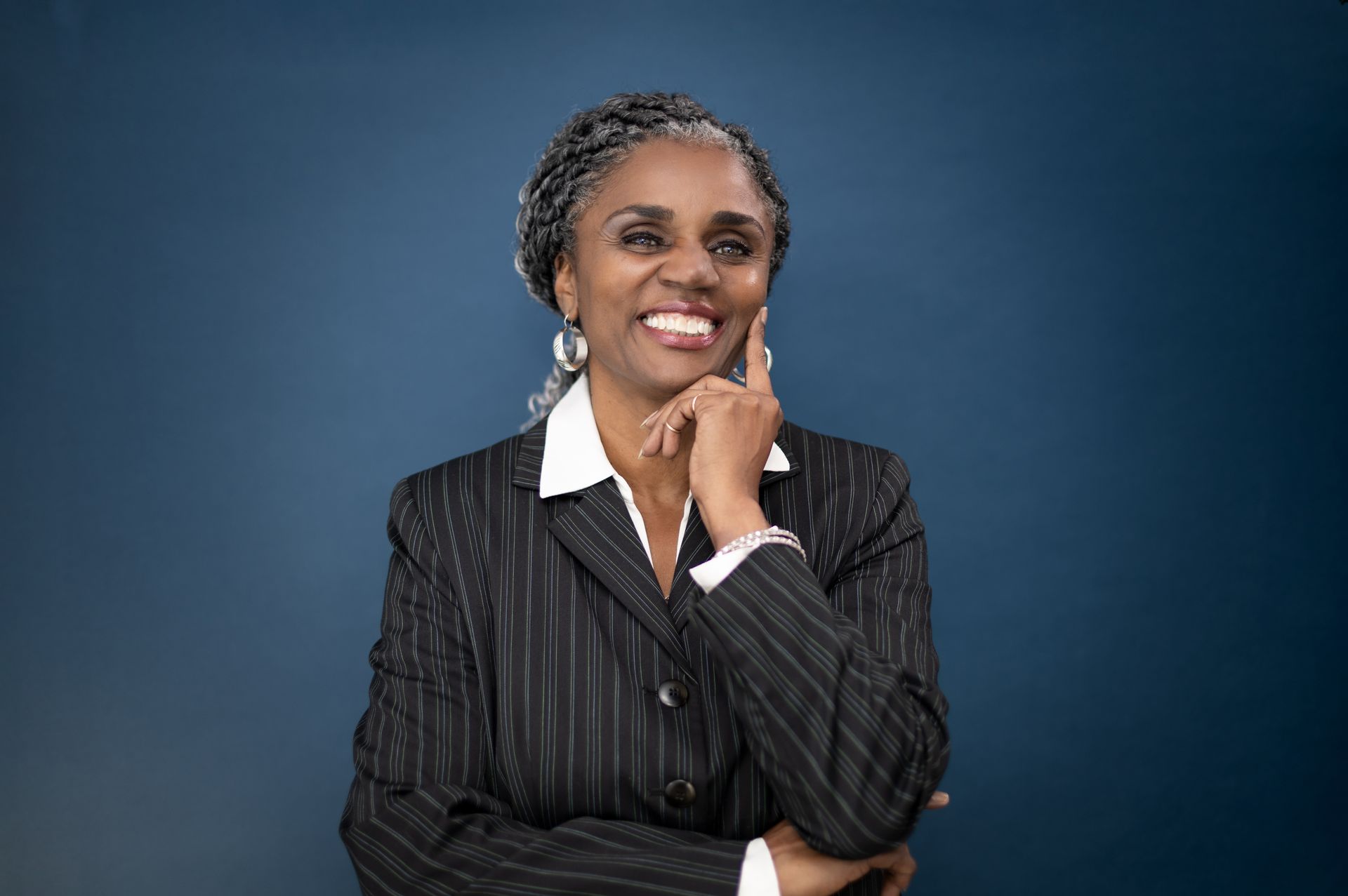A woman in a suit is smiling with her hand on her chin.