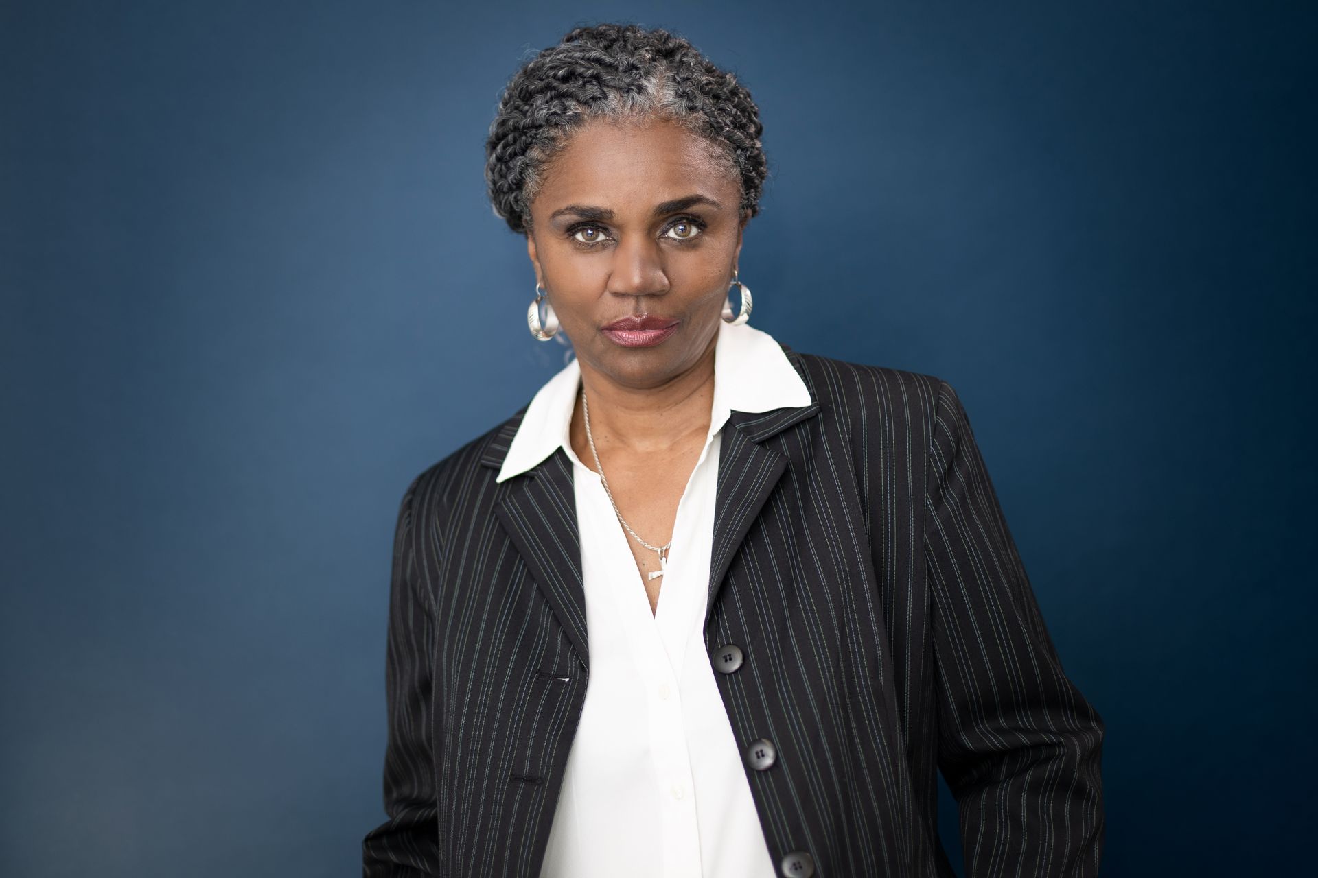 A woman in a suit and white shirt is standing in front of a blue wall.