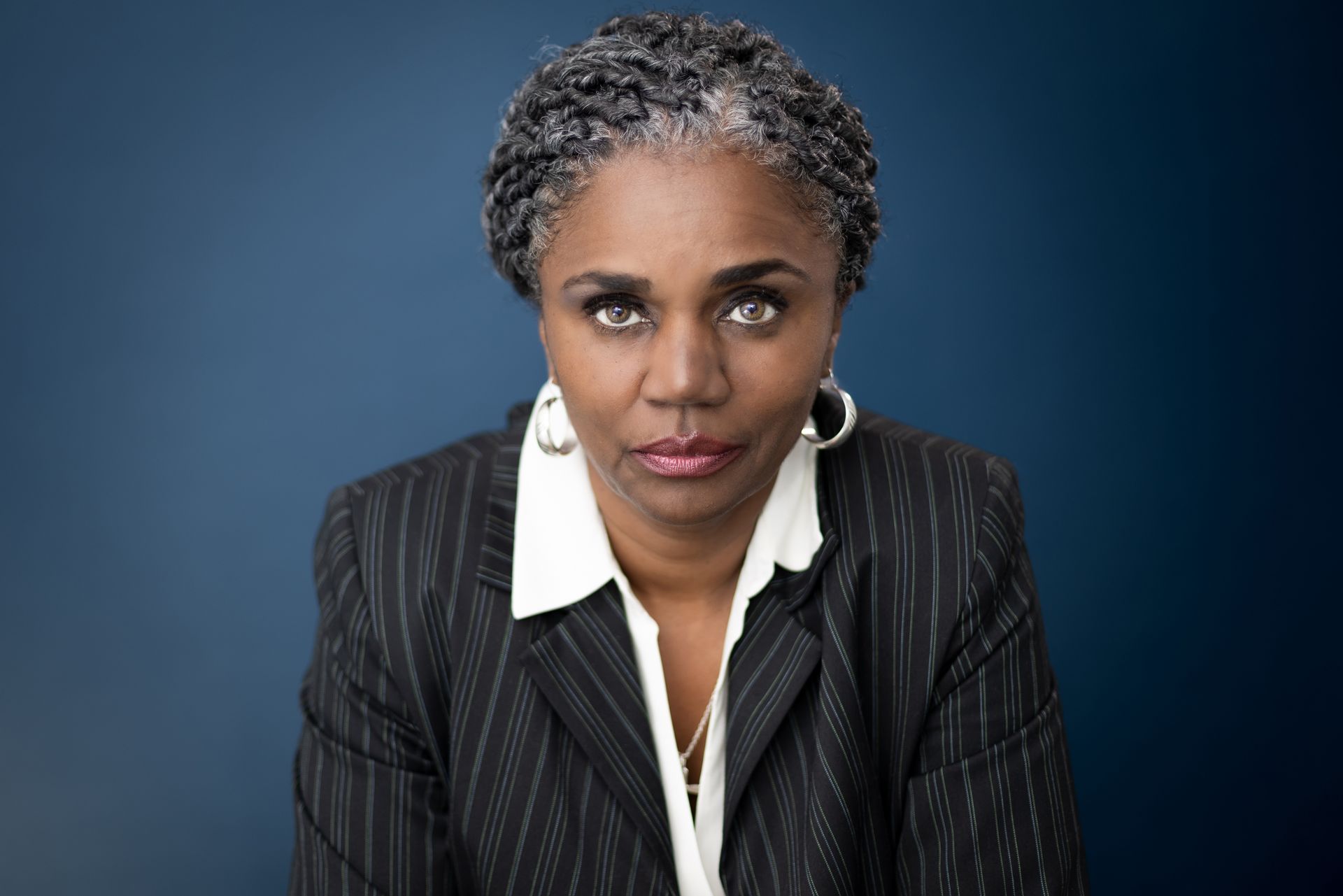 A woman with gray hair is wearing a suit and earrings