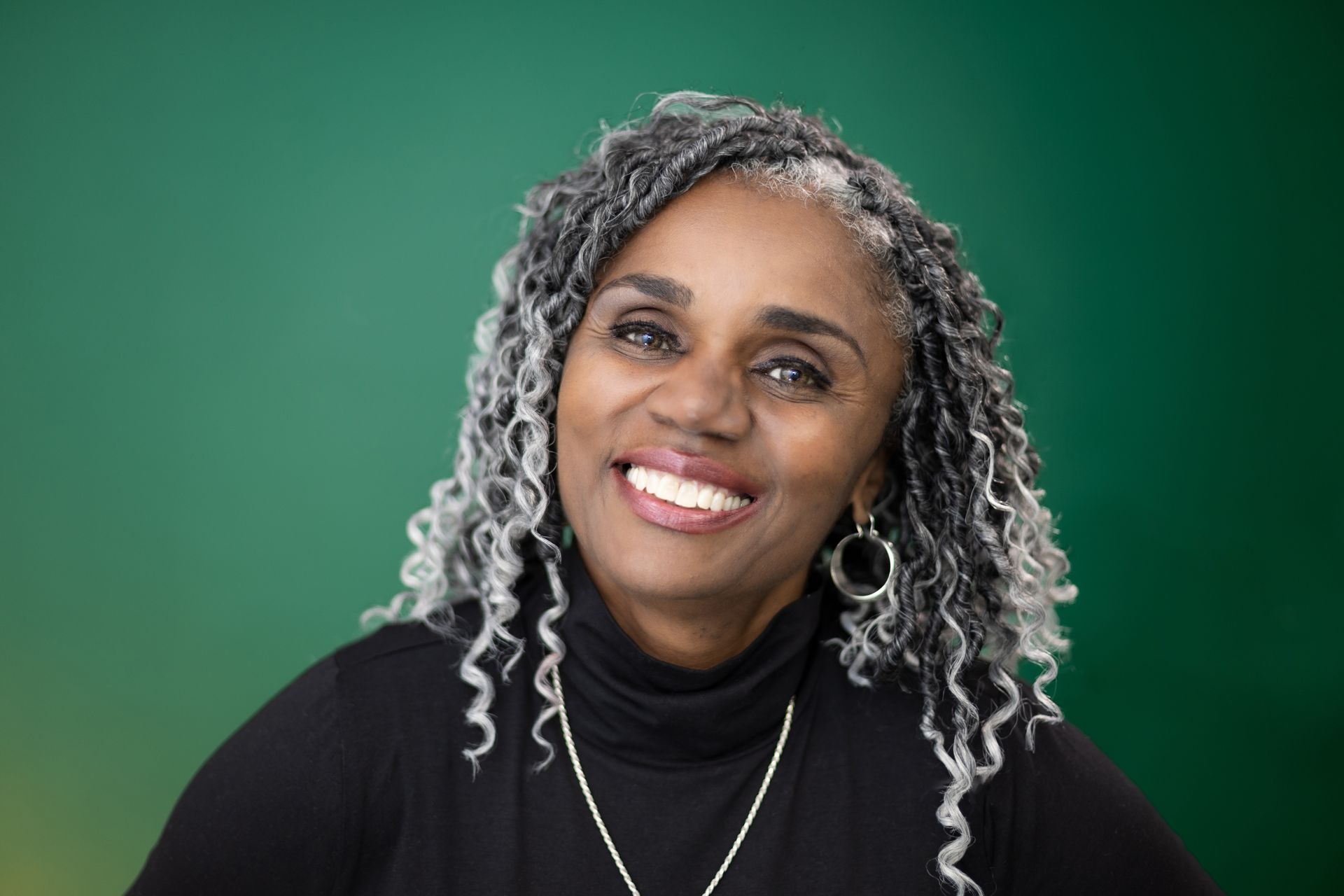 A woman with gray hair and dreadlocks is smiling for the camera.