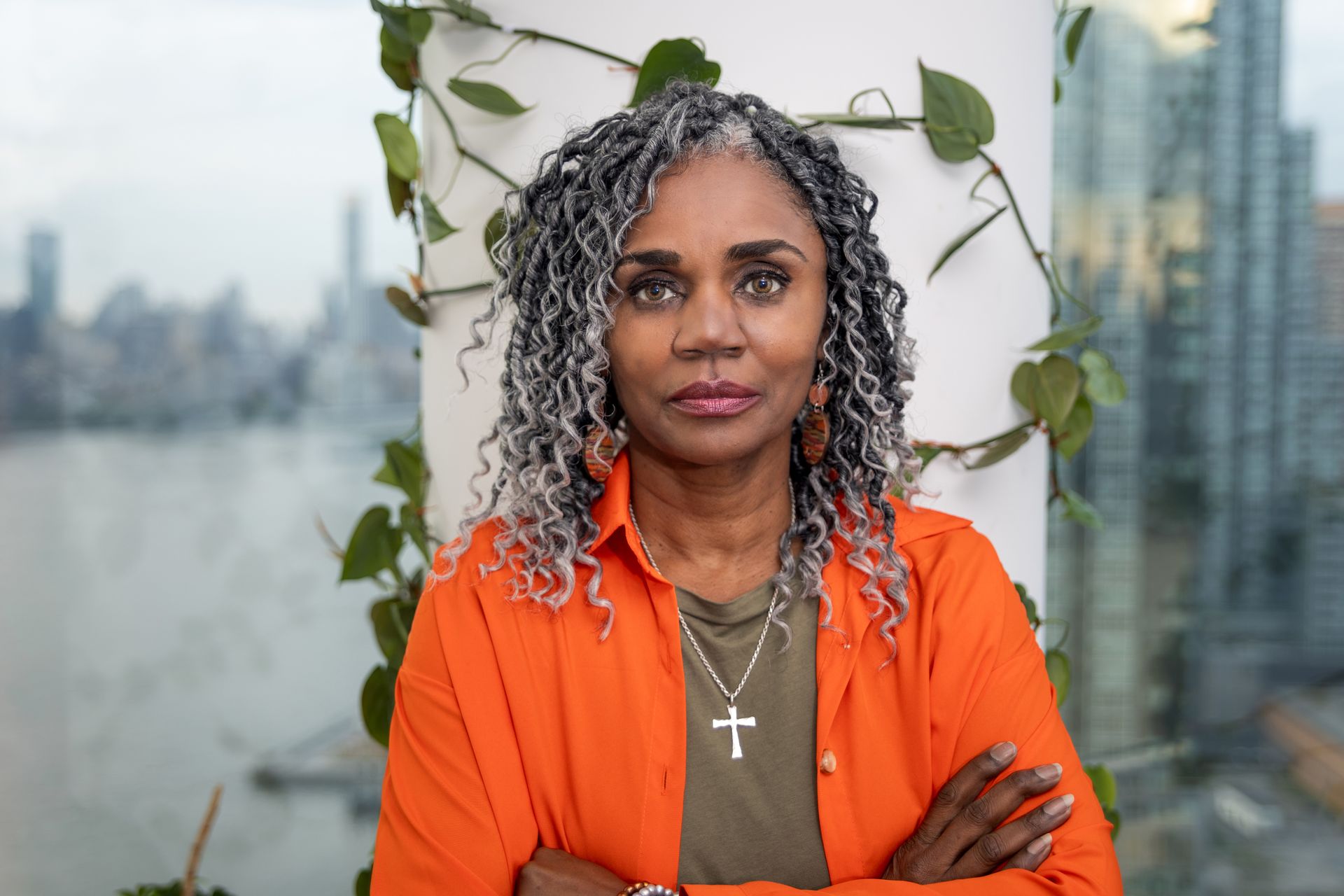 A woman with gray hair and a cross necklace is standing with her arms crossed.