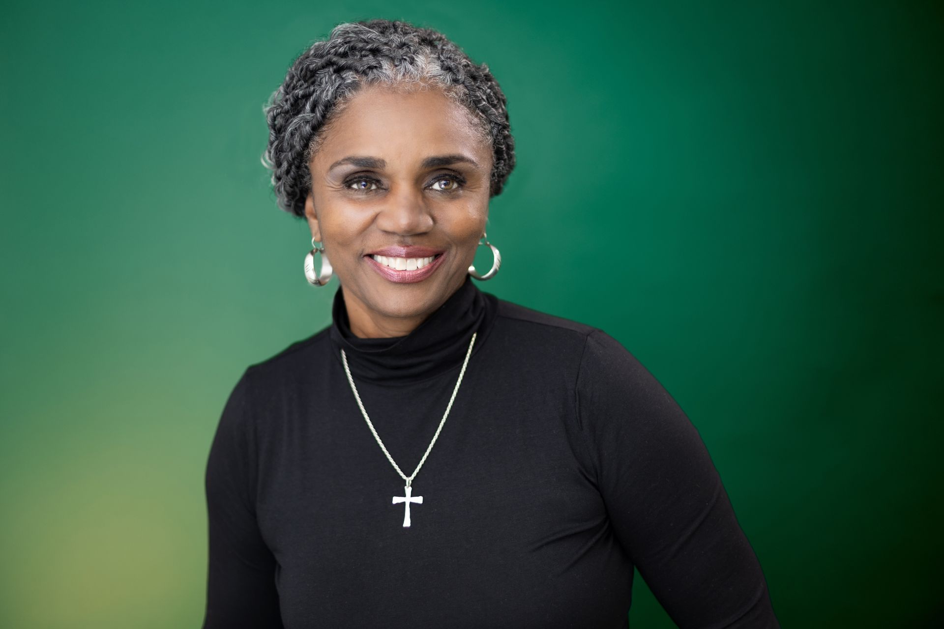 The woman is wearing a black turtleneck and a cross necklace.