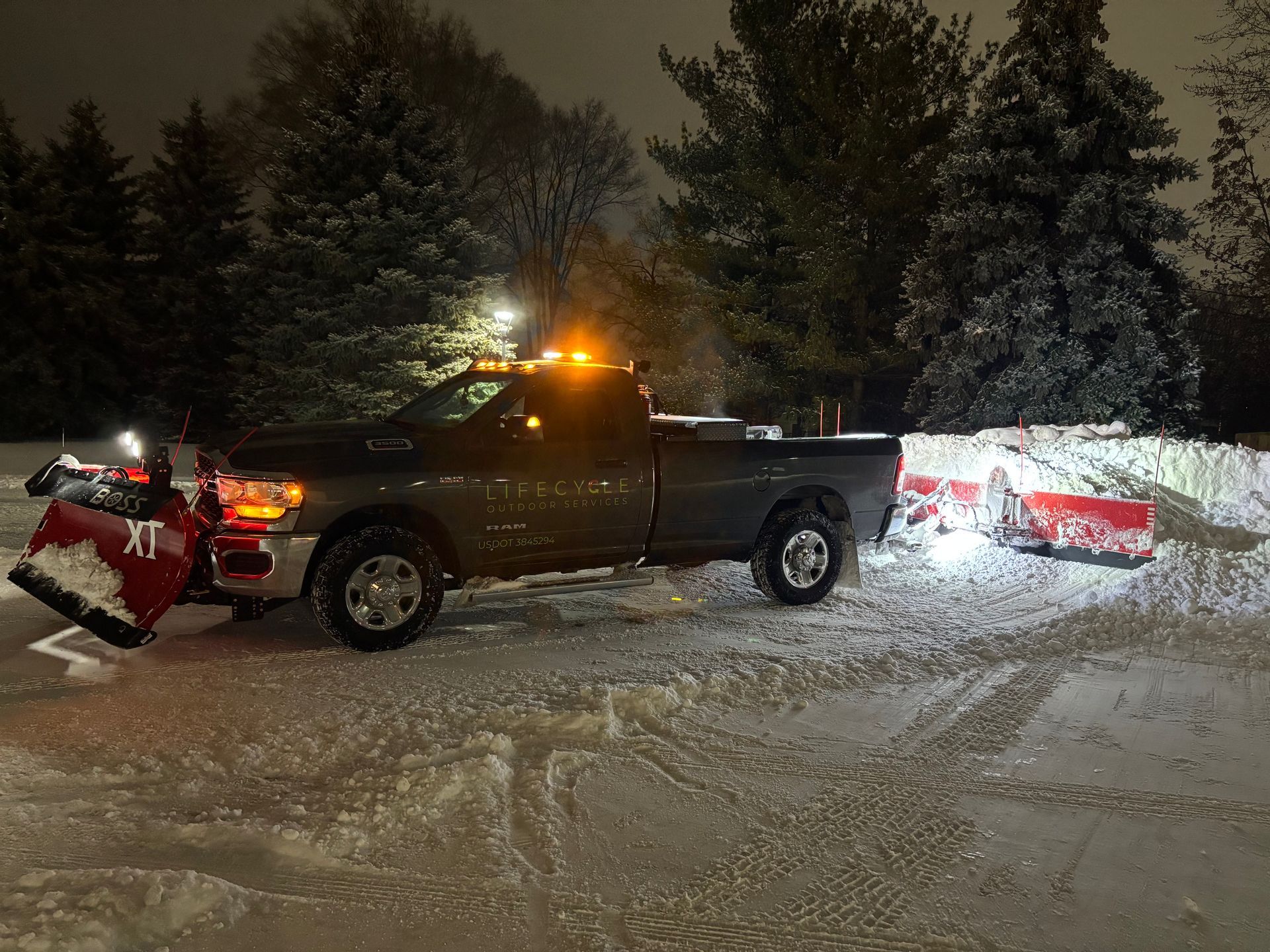 Snowplow truck clearing snow at night. Red plow blade and lights on.