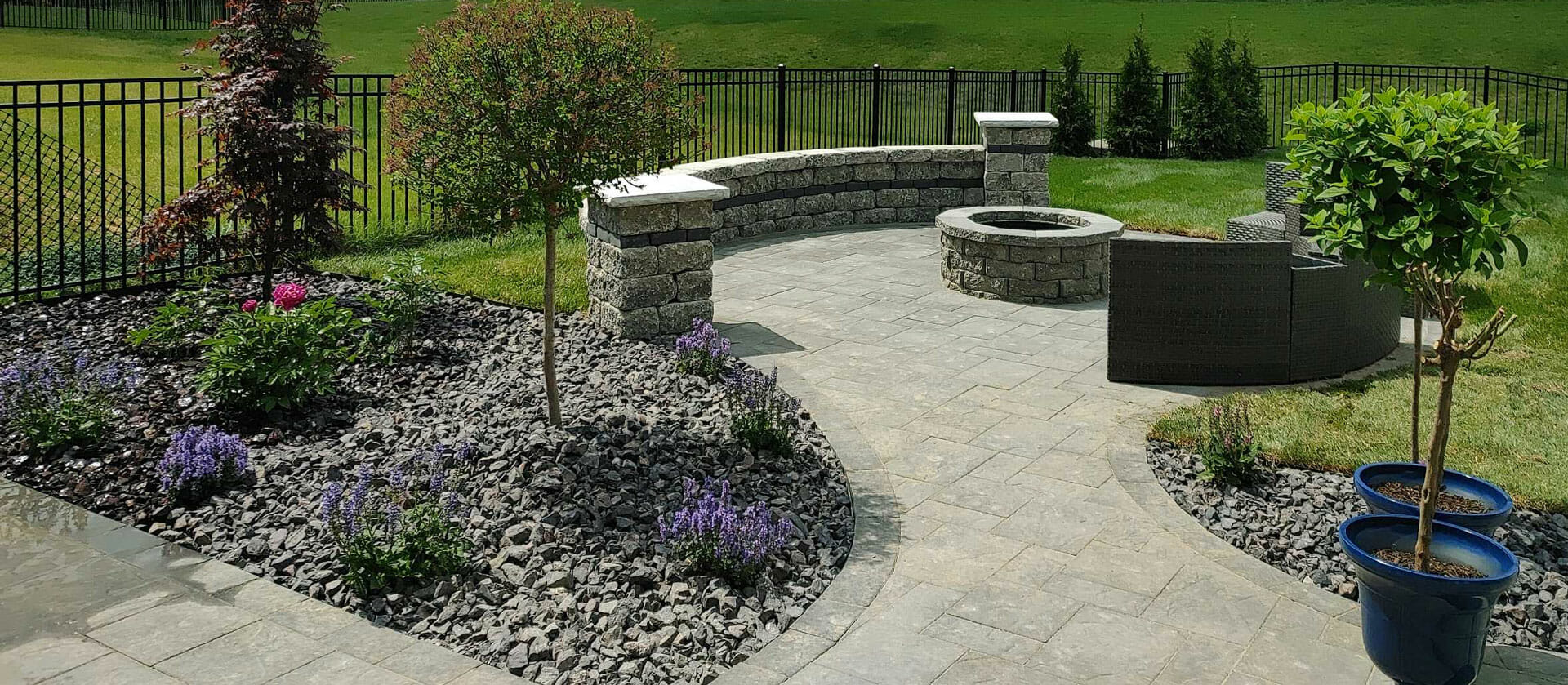 Landscaped backyard with stone pathway, seating, fire pit, and planted trees.