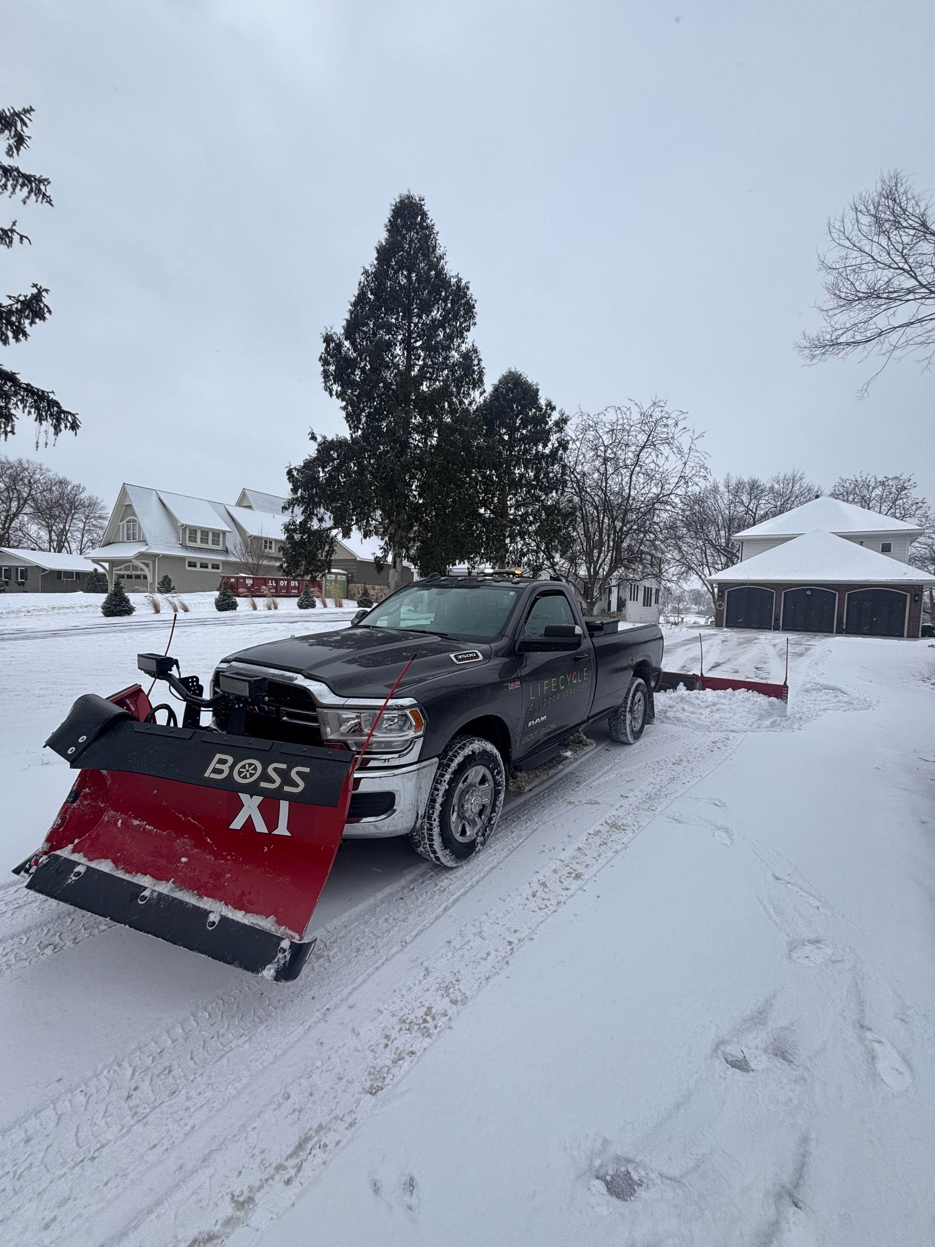 Black pickup truck with a red snowplow plowing a snow-covered street. Winter scene.