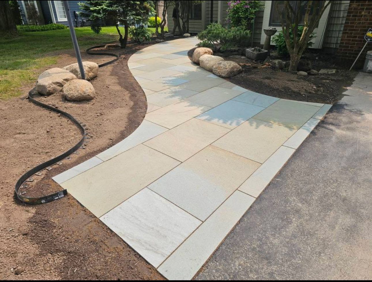 Stone walkway curves past landscaping to a house, with a black border.
