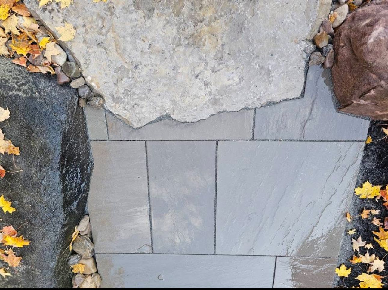 Stone walkway flanked by large rocks and fallen yellow leaves.
