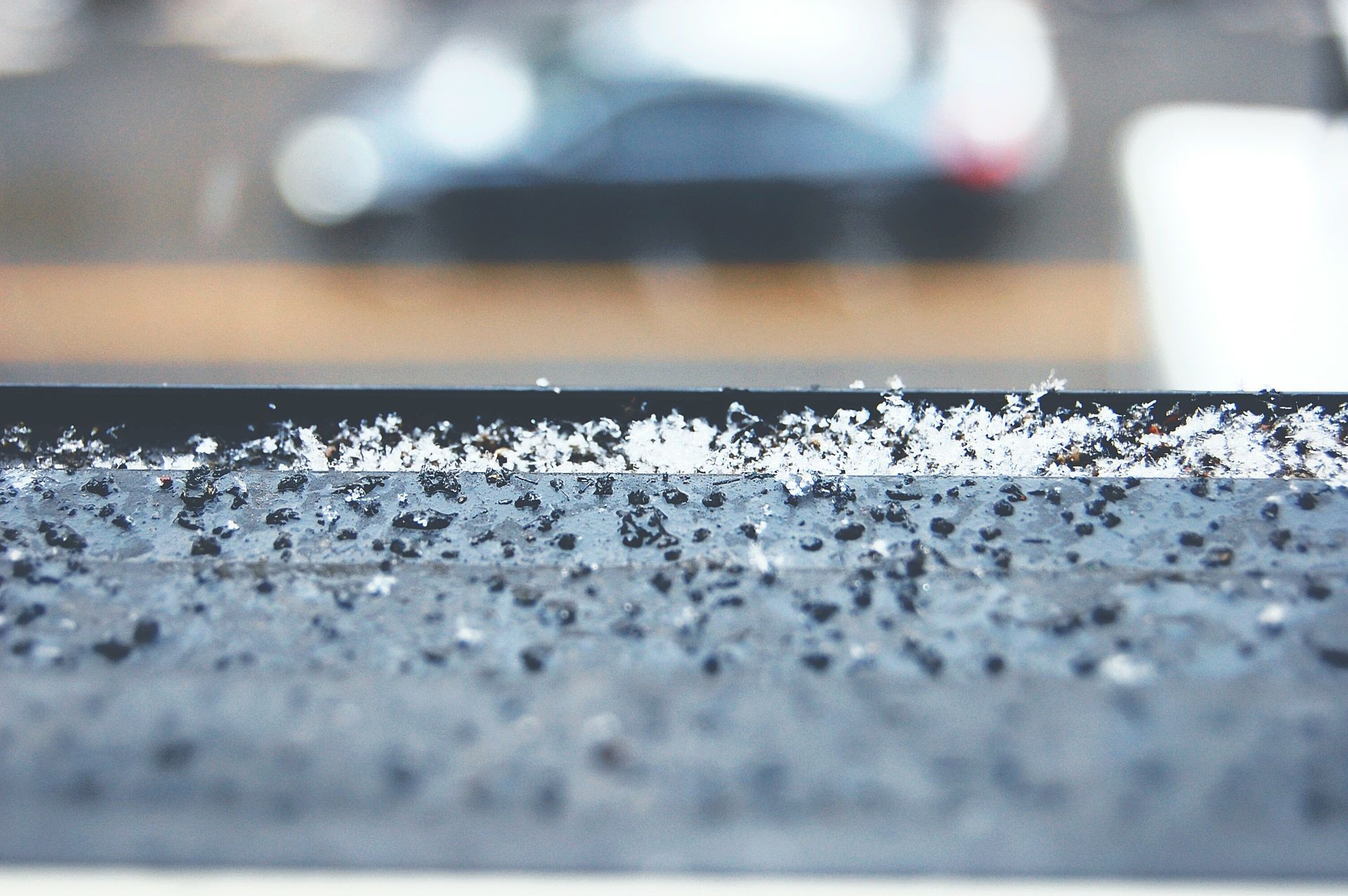 Snow and grit on a window ledge, with a blurry street and car in the background.