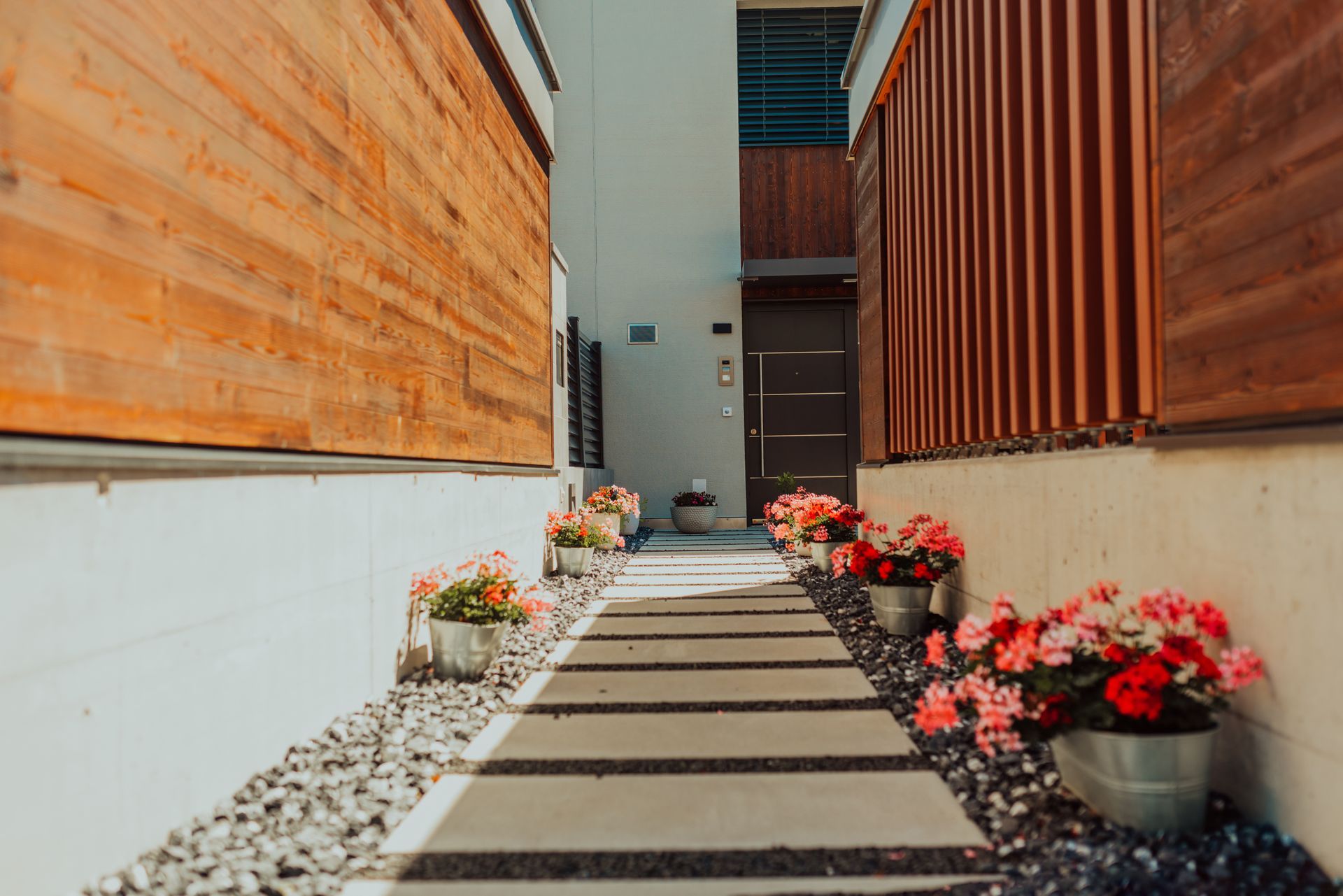 A pathway between two buildings with flowers in pots on the side.