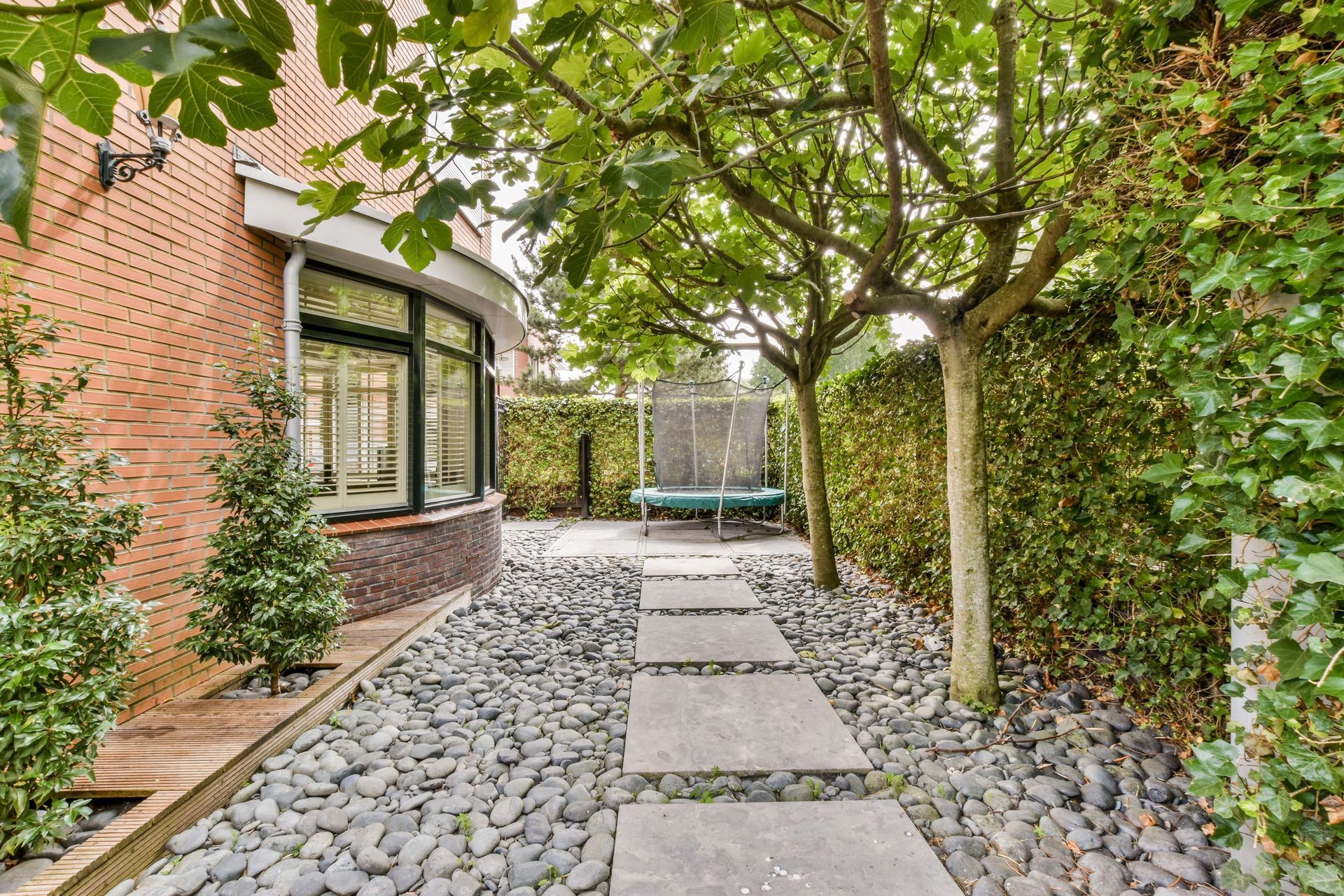 There is a trampoline and a pathway in the backyard of the house.