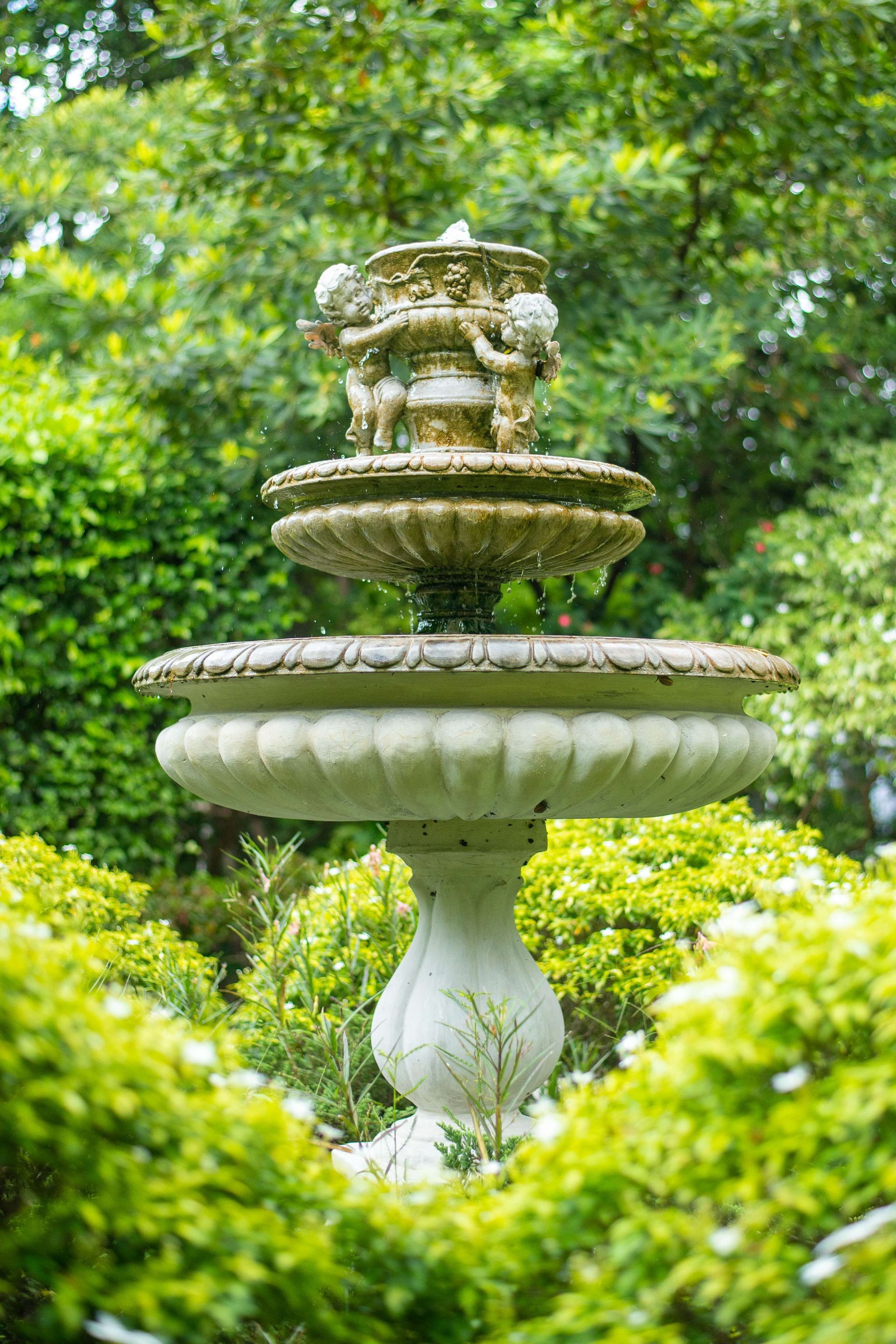 A fountain with cherubs on top of it in a garden surrounded by trees.
