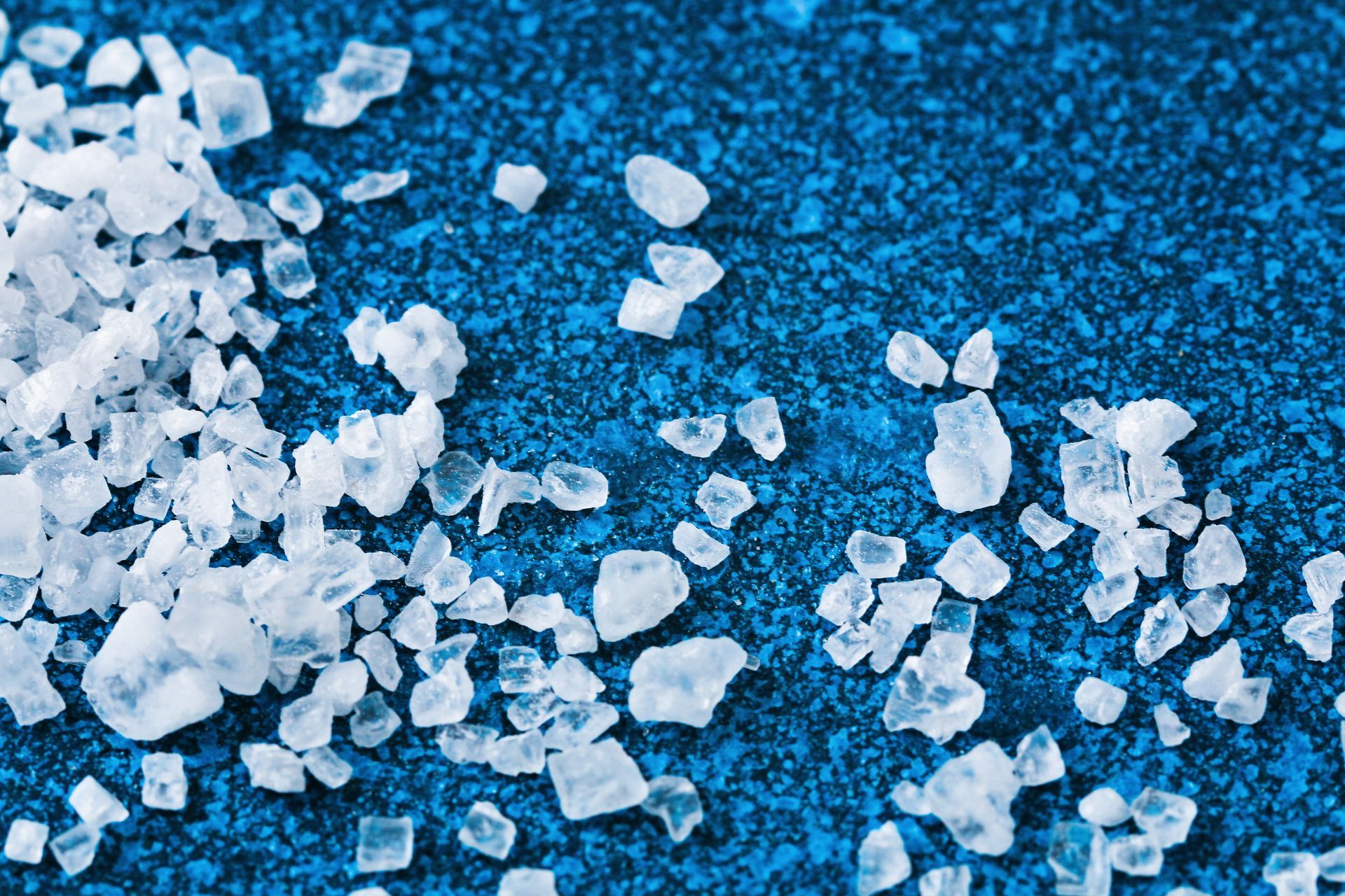 Coarse white salt crystals scattered on a textured blue surface.