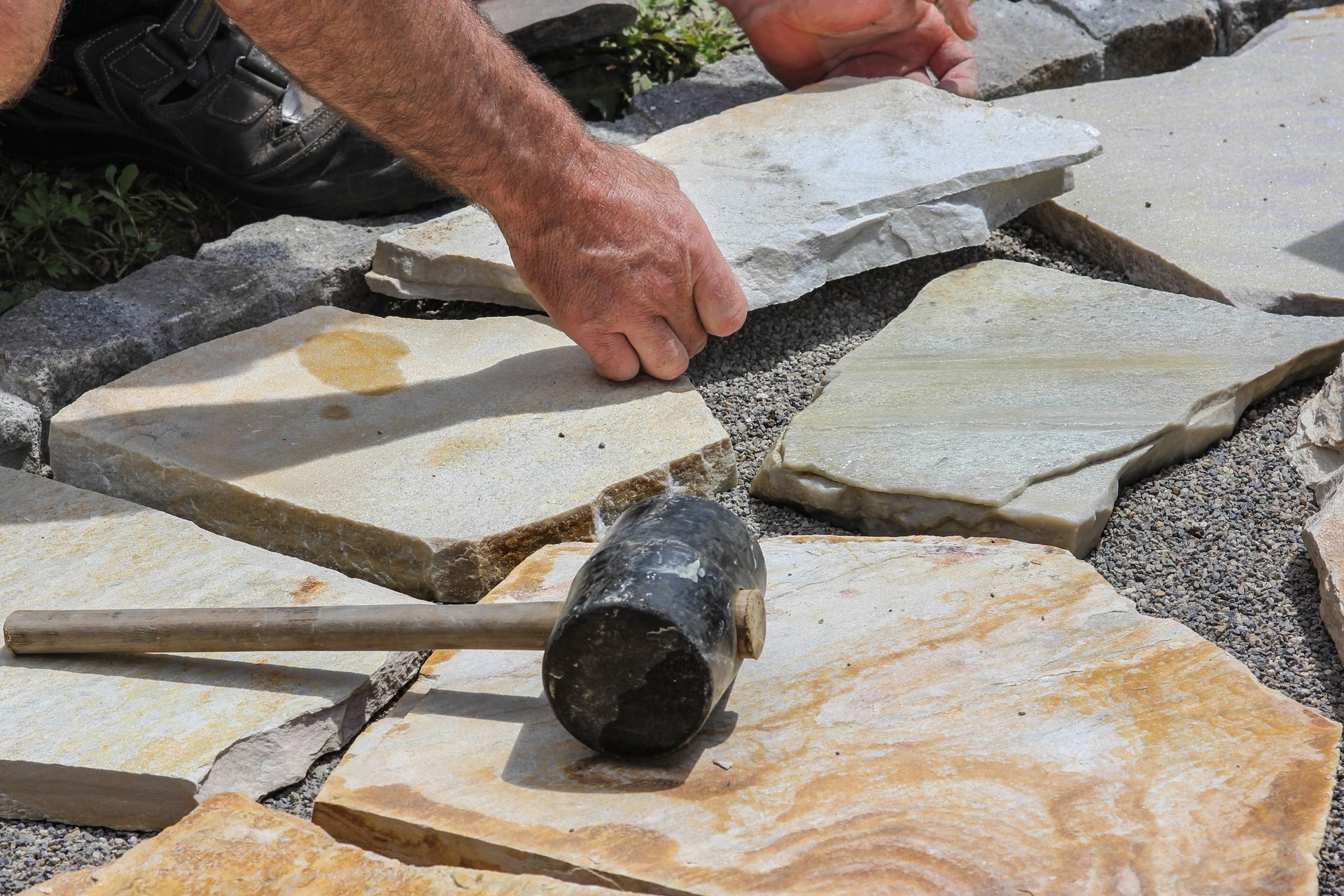 A man is laying a stone walkway with a rubber mallet.