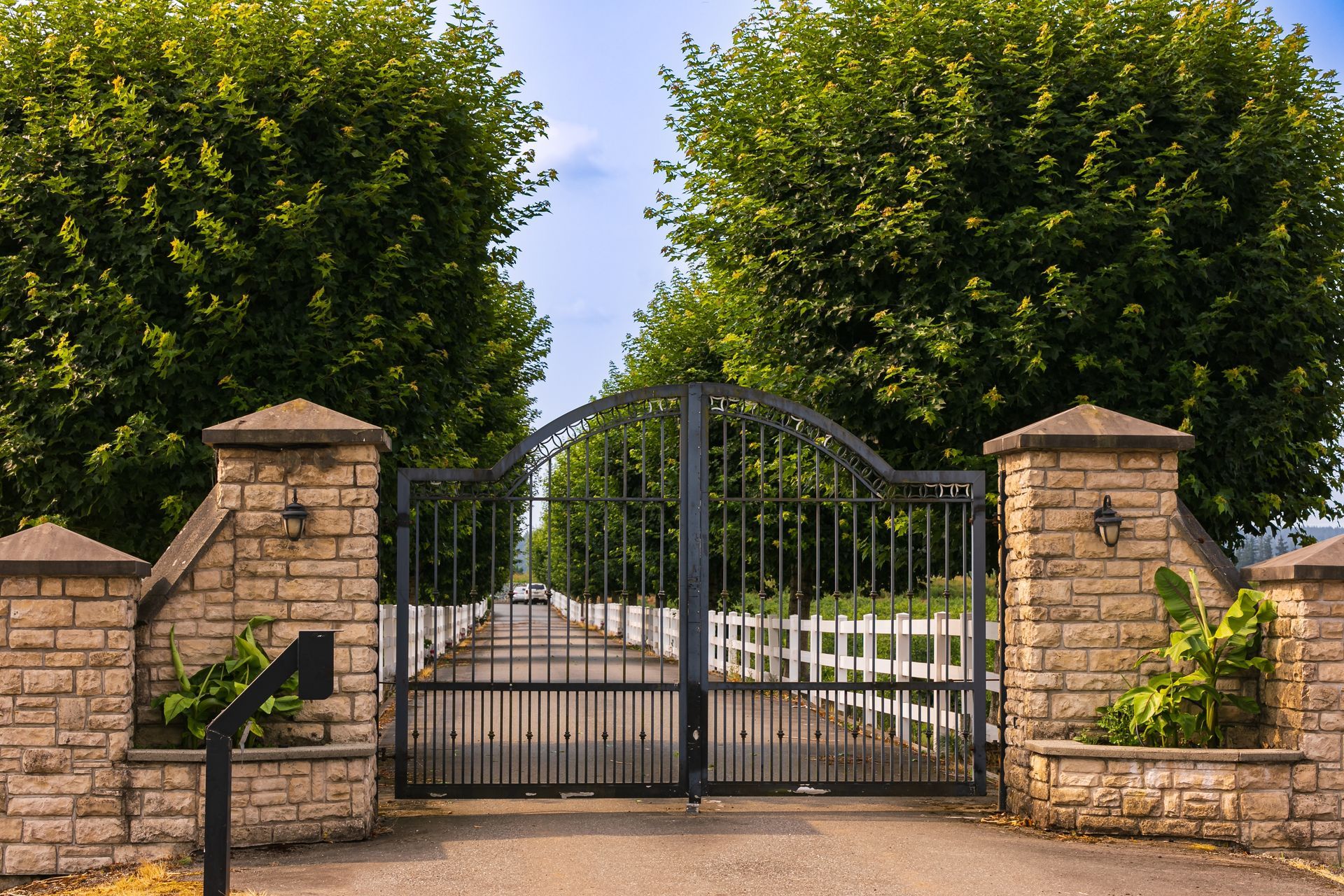 A wrought iron gate is surrounded by brick pillars and trees