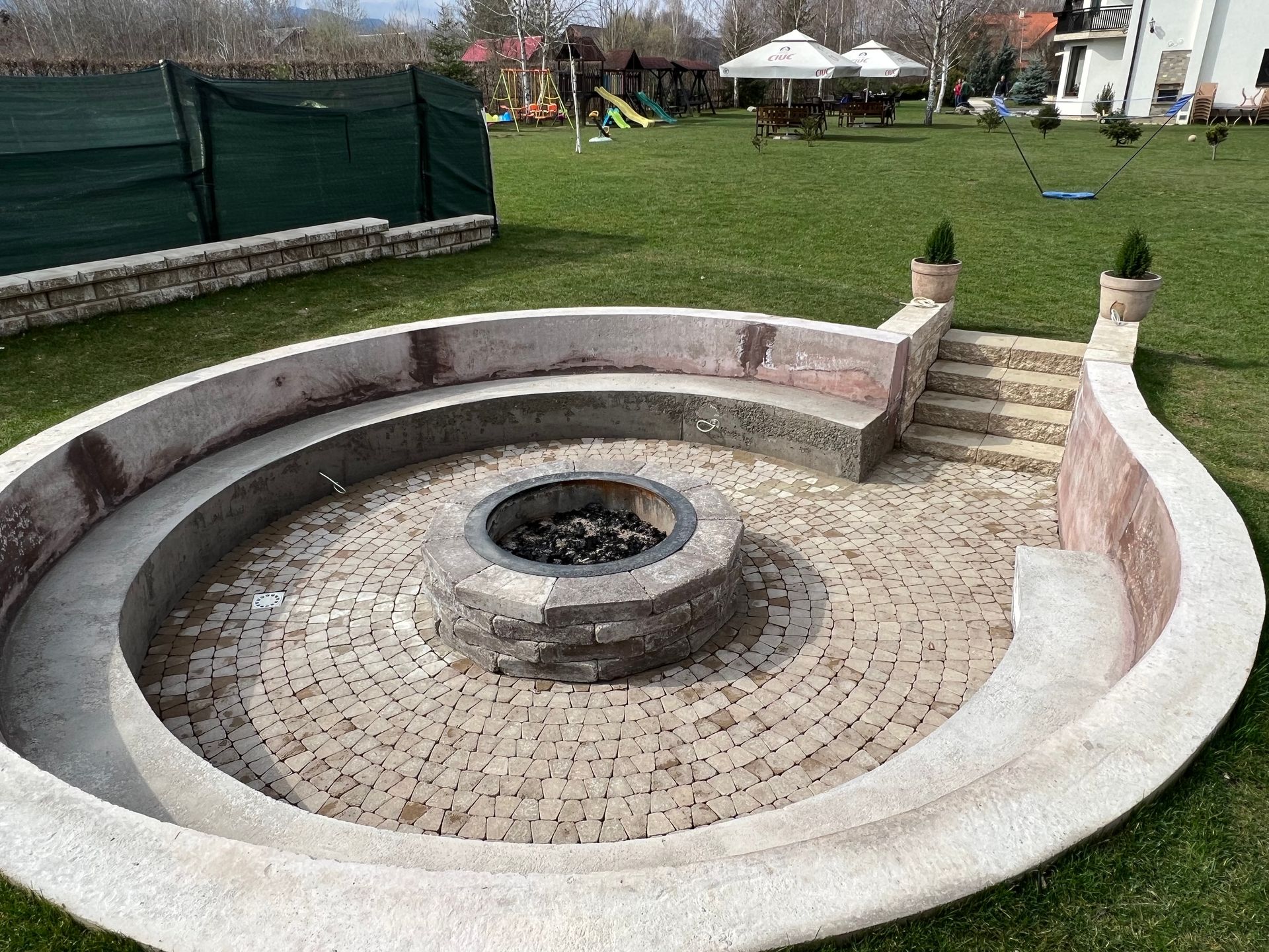 Circular fire pit with stone seating area in grassy backyard.