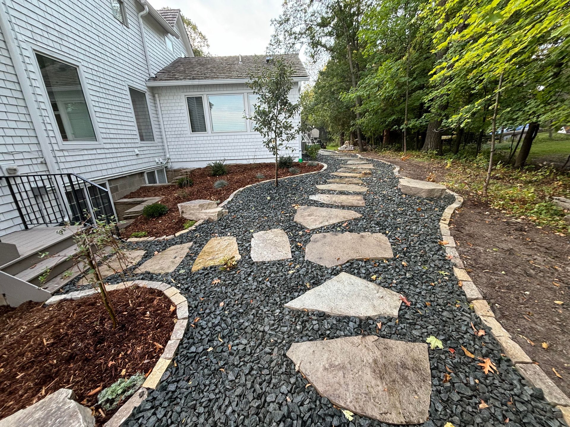 Stone path through a landscaped yard with black gravel and a white house.