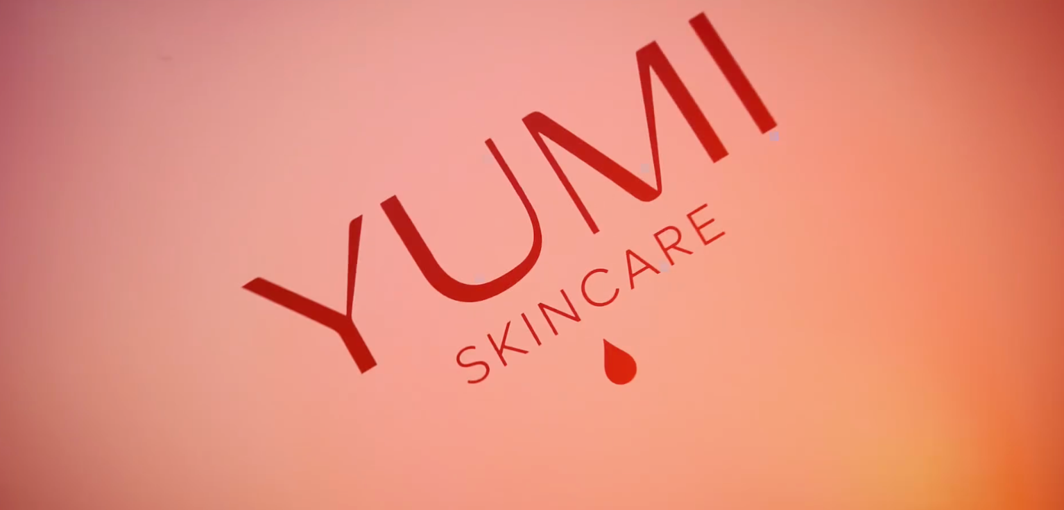 Un gros plan d'un logo de soins de la peau Yumi sur un fond rose.