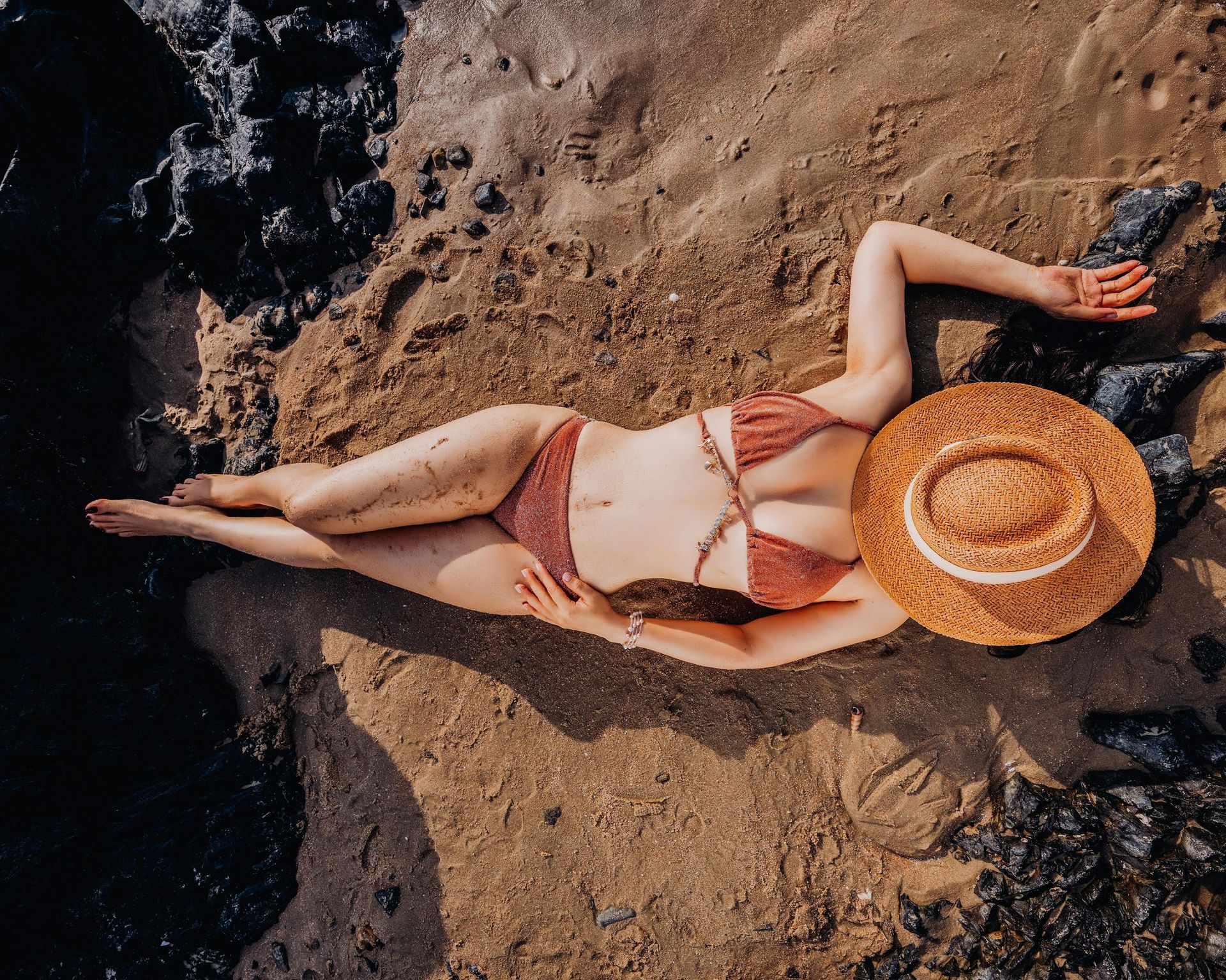 Une femme en bikini et chapeau de paille est allongée sur la plage.