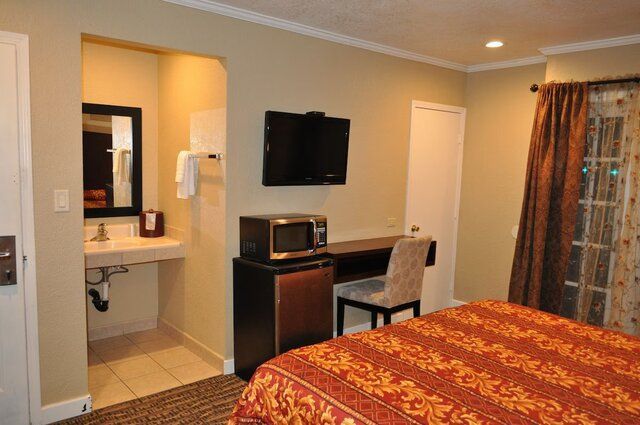 Hotel room with a bed, desk, microwave, TV, and open bathroom.