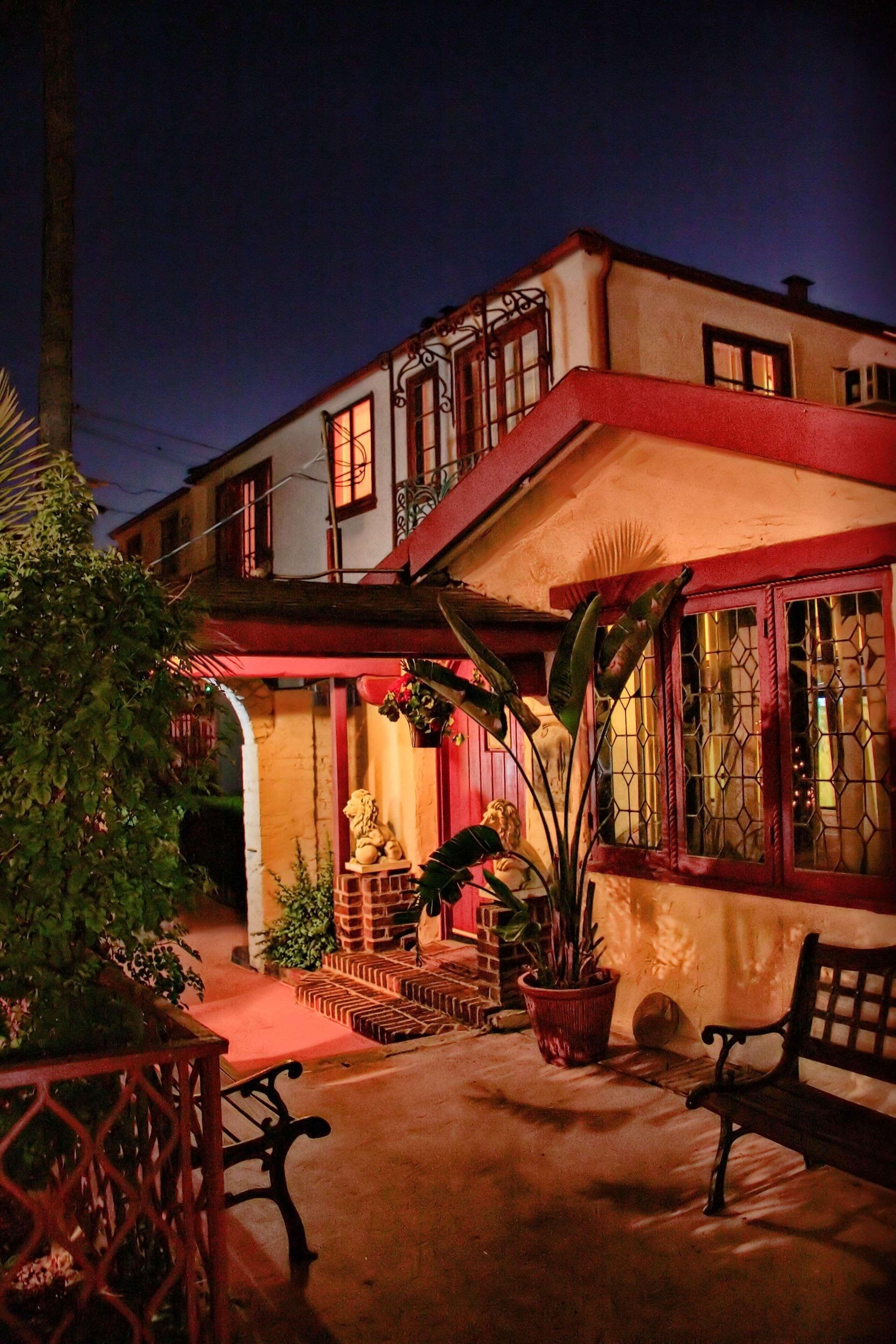 Courtyard of a building at night. Red trim accents the cream walls and dark windows. A bench sits in the foreground.